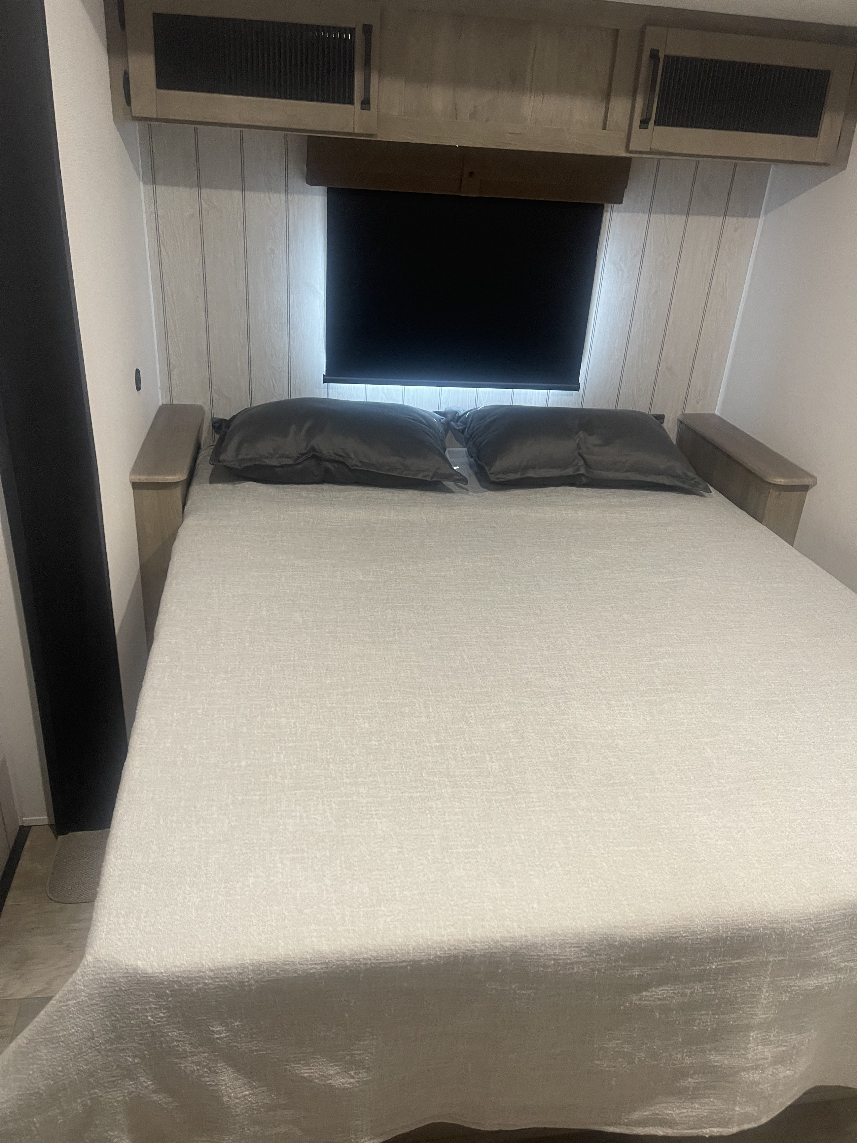 RV rental bedroom: a bed with light bedding, dark pillows, overhead cabinets, wood paneling, and a window blind.. Forest River Palomino Puma 2025