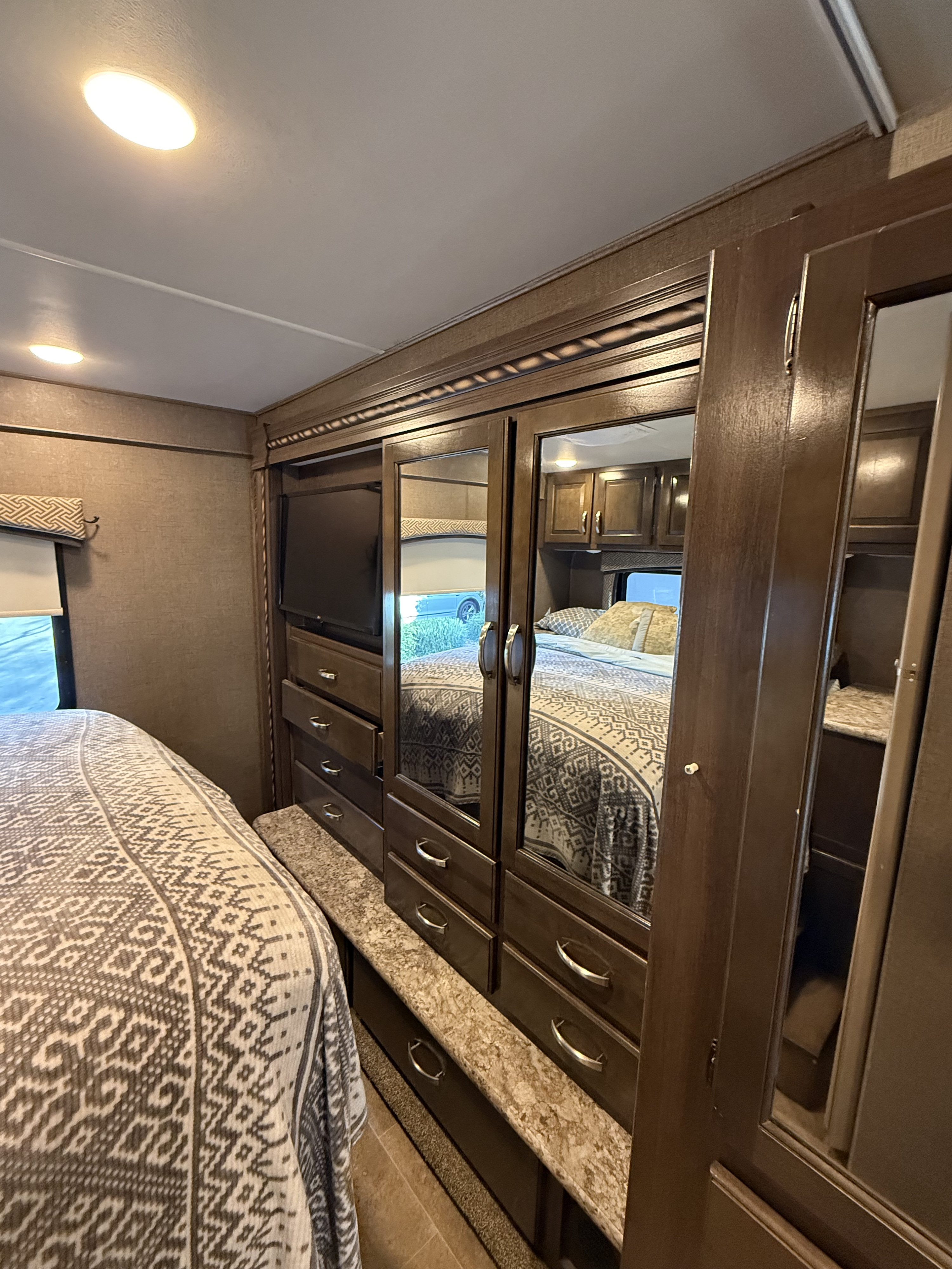 RV rental bedroom with a built-in wardrobe, mirrored doors, TV, and drawers next to a bed with a patterned spread.. Thor Chateau 2017