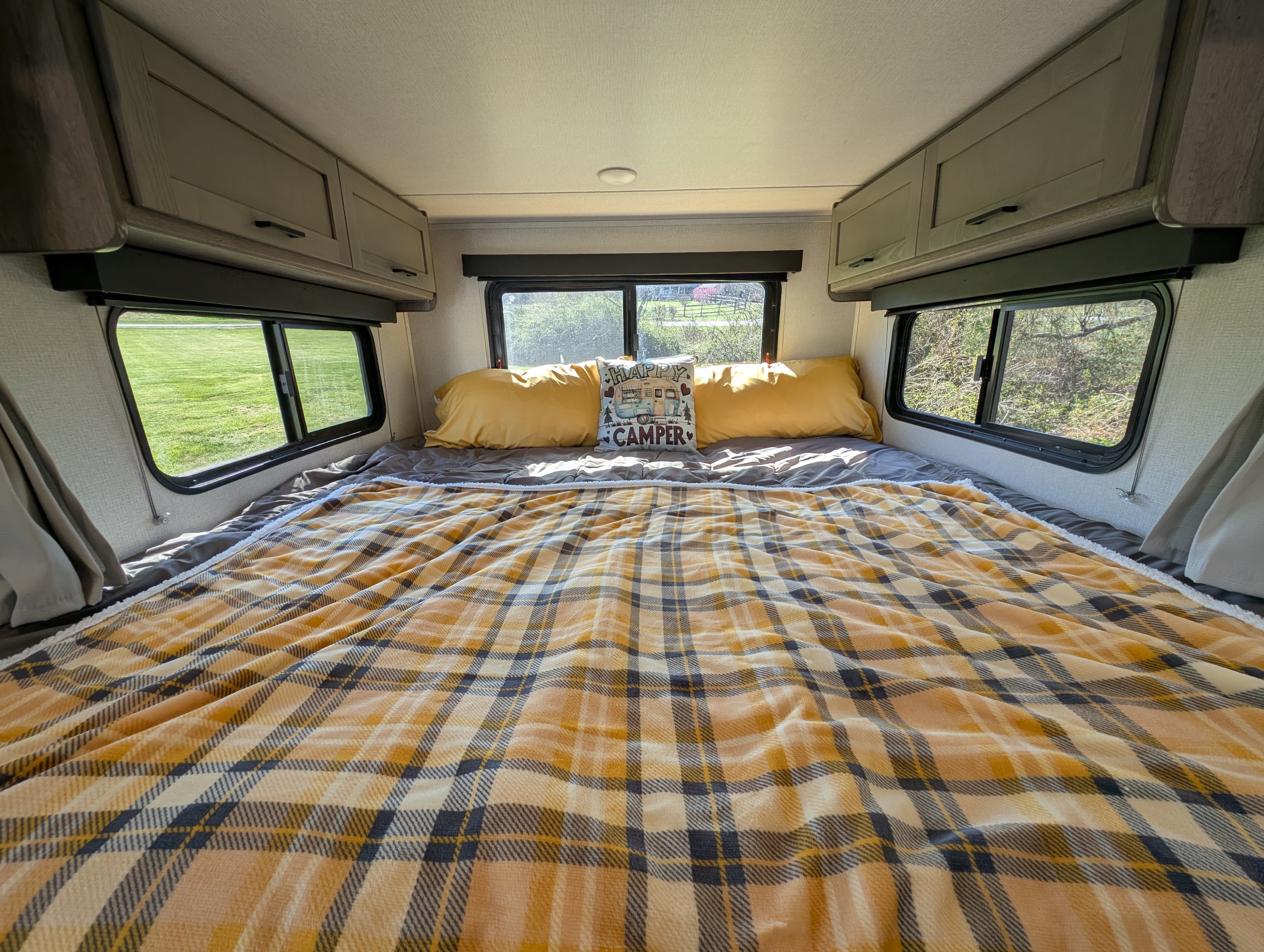 Cozy RV rental bedroom with a yellow plaid blanket, comfy pillows, and scenic window views, perfect for your next camping trip.. Keystone Outback Ultra Lite 2021