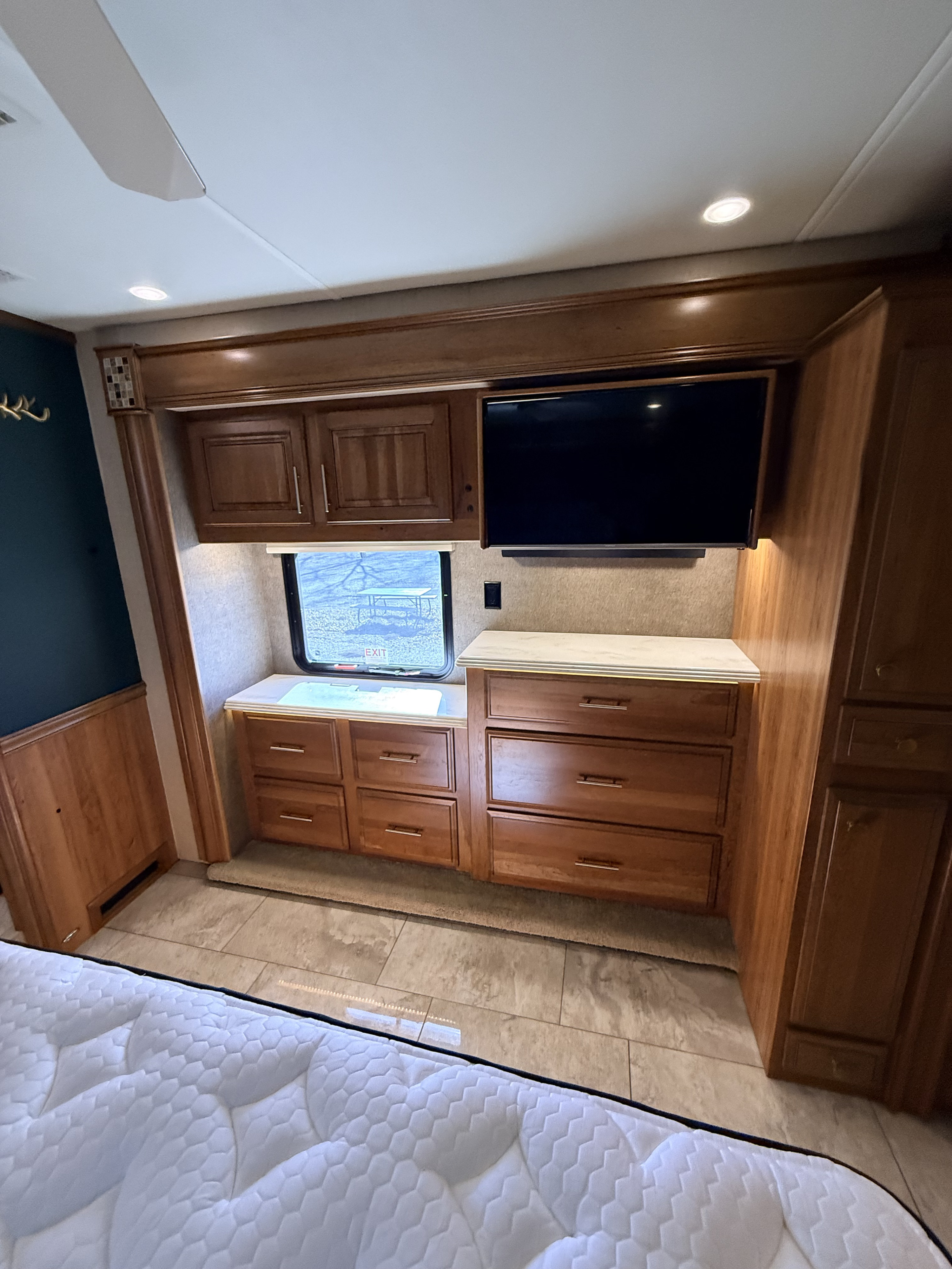 RV rental bedroom with sleek wood cabinets, a wall-mounted TV, window view, and comfy mattress for travelers.. Entegra Coach Aspire 2018