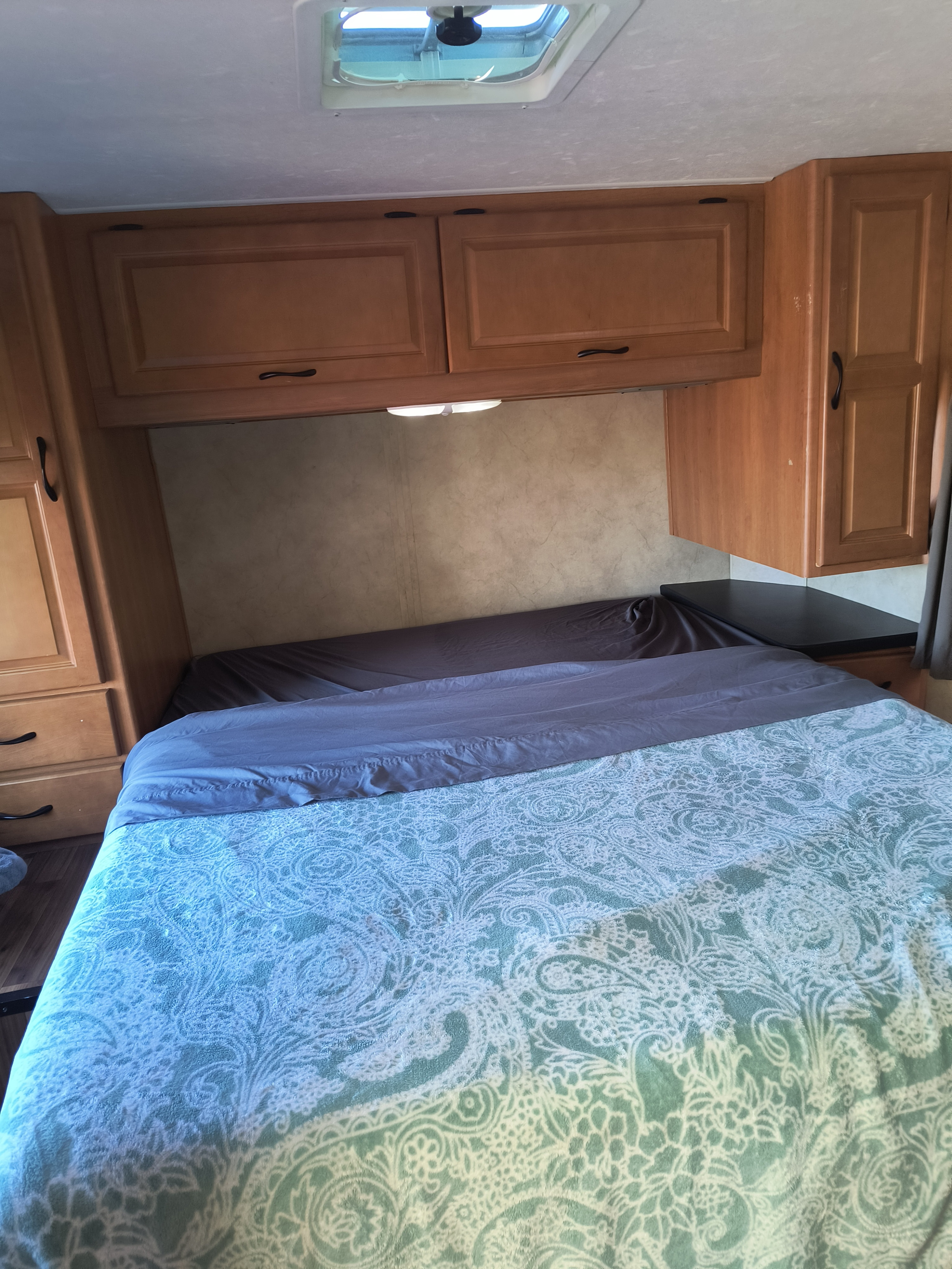 RV rental bedroom: a cozy bed with a patterned blanket, overhead storage cabinets, and a ceiling vent for comfortable travel.. thor majestic 2014