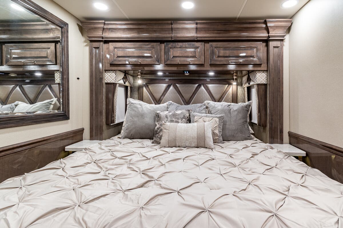 Comfortable RV rental bedroom with a plush bed, throw pillows, and stylish wooden cabinetry above the upholstered headboard.. Entegra Coach Anthem 2020