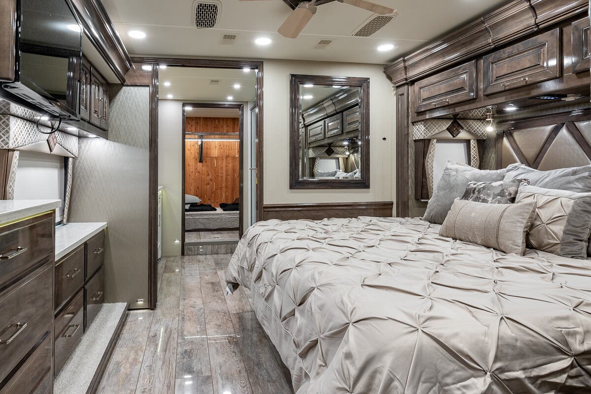 This opulent RV rental bedroom offers a comfortable bed, rich wood cabinetry, and integrated lighting for luxury travel.. Entegra Coach Anthem 2020