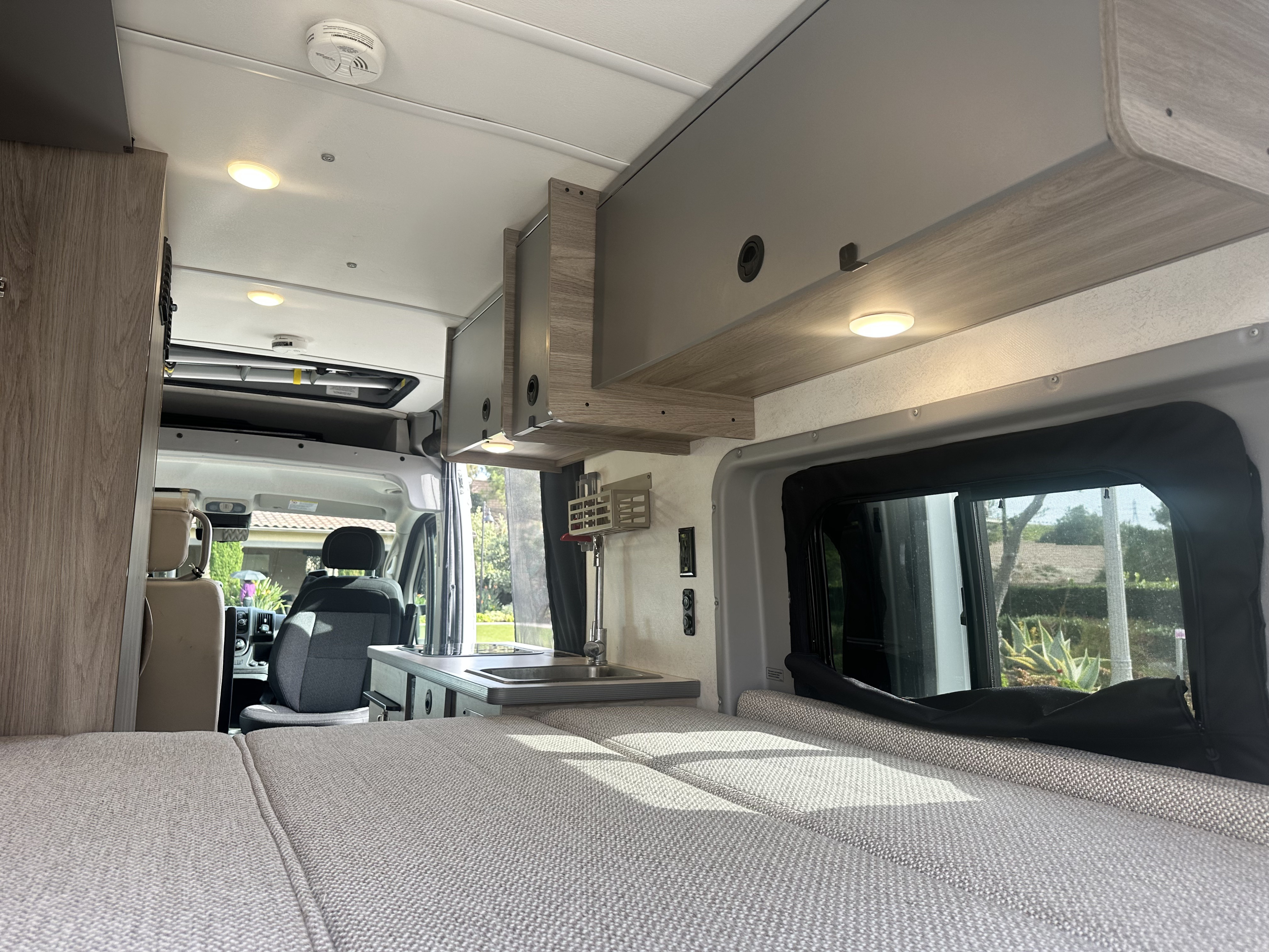 Bright rv rental interior featuring a comfy bed, overhead storage, and a functional kitchenette, ready for adventure.. Winnebago Solis 2022