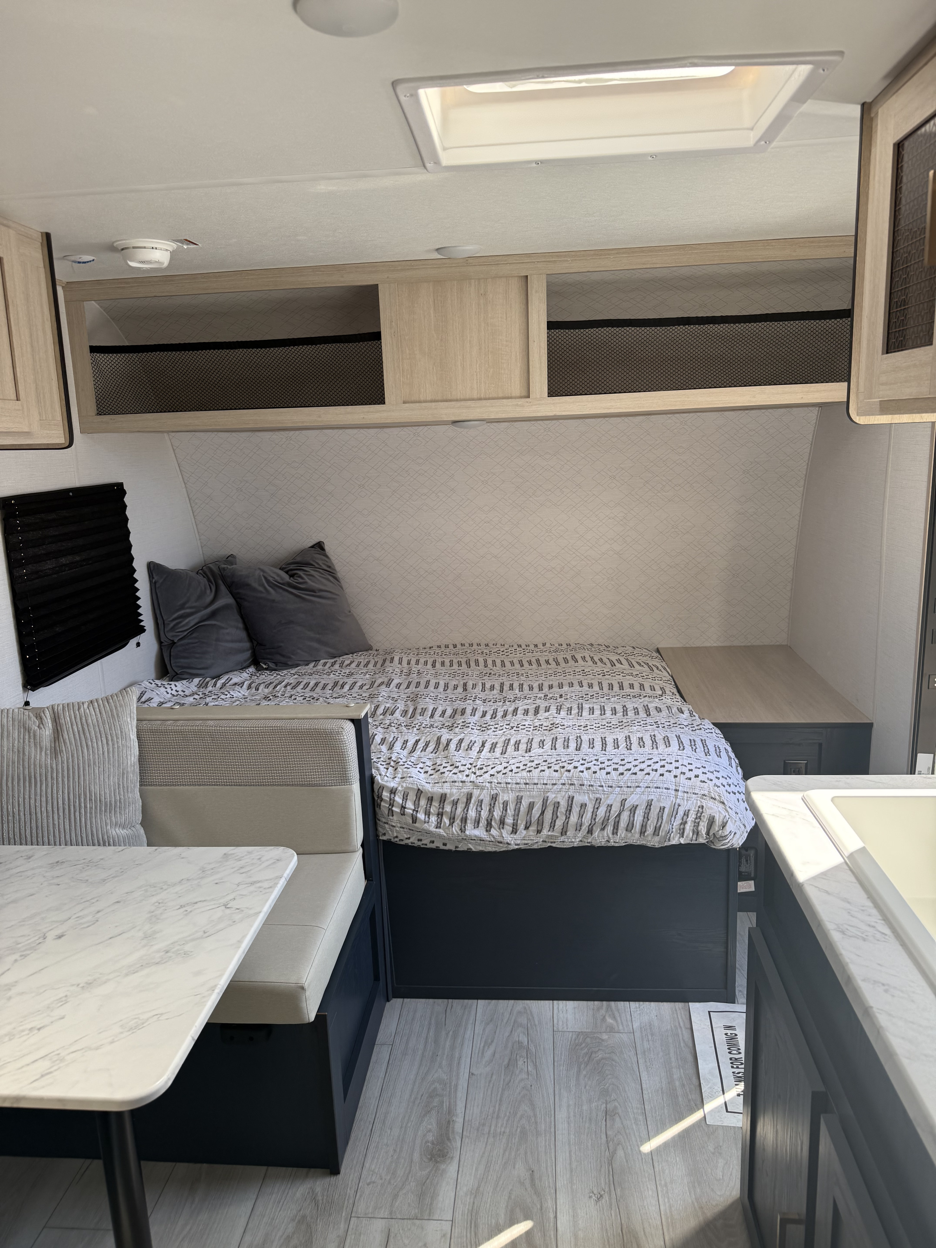Modern RV rental interior with a cozy bed, dinette, overhead storage, and kitchen counter. Bright and functional for travel.. Forest River Avenger LT 2025