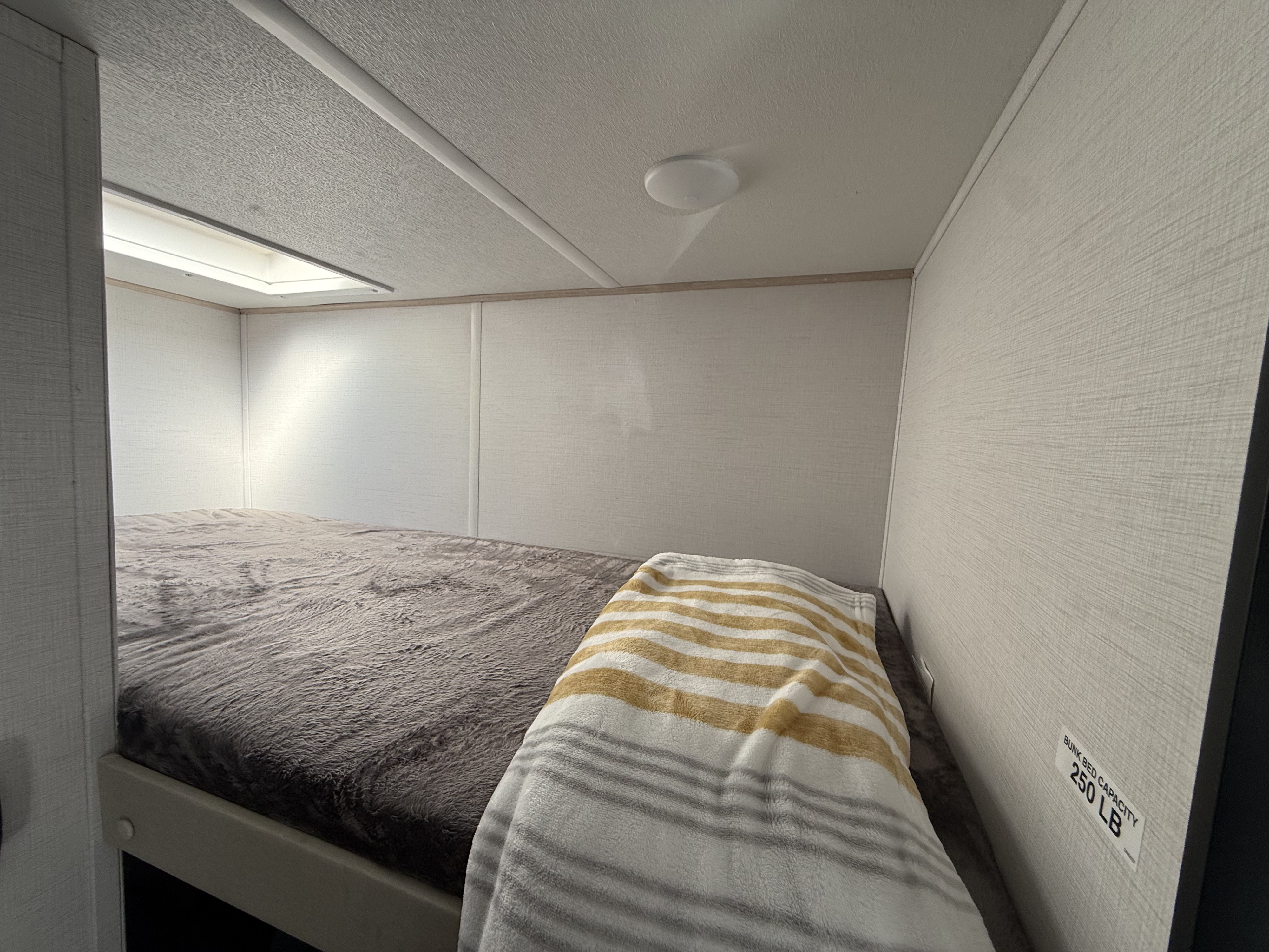 RV rental interior featuring a cozy bunk bed with soft blankets and a 250 LB capacity.. Forest River Avenger LT 2025