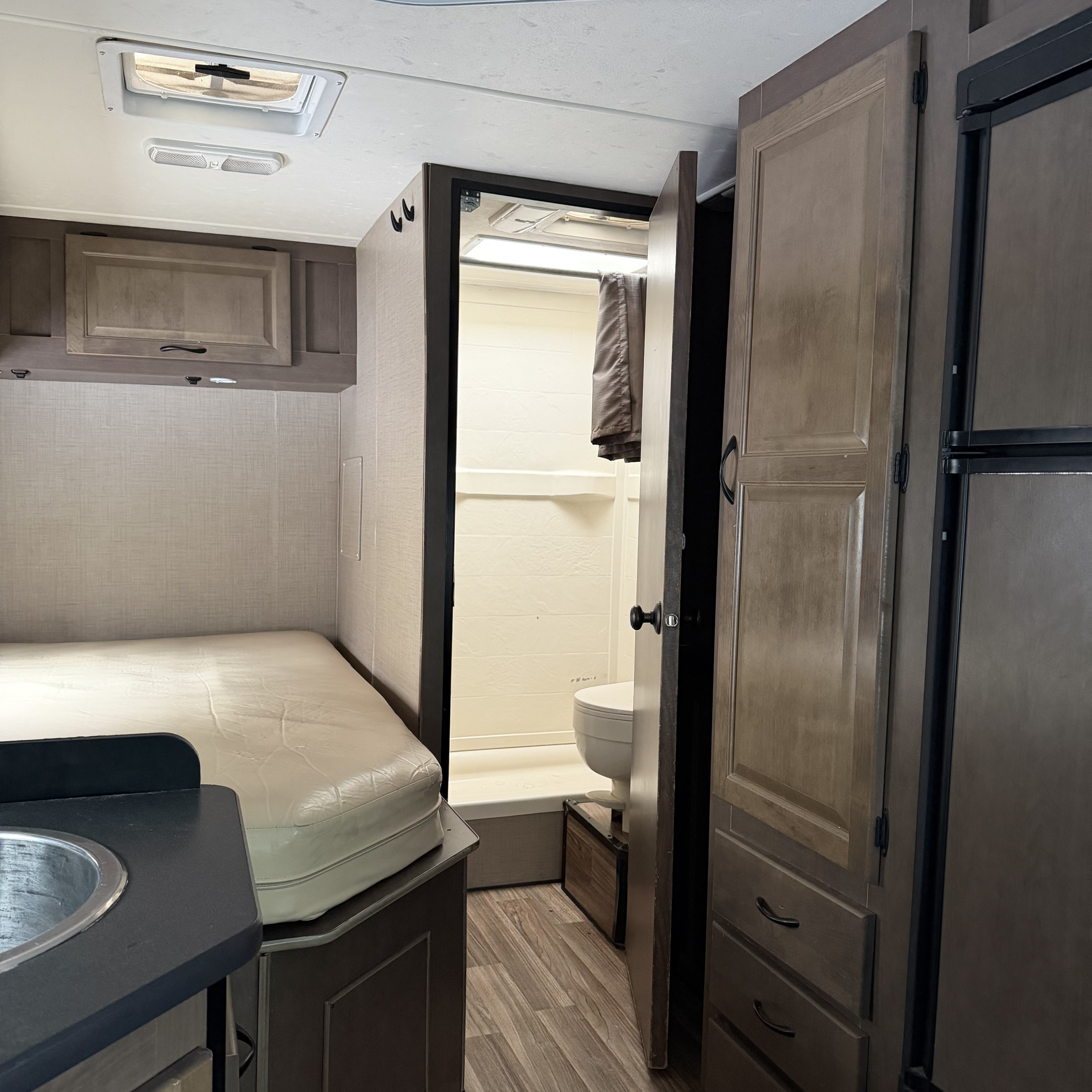 Compact RV rental interior showing a bed, small sink, and an open door to the bathroom with a toilet and shower.. Thor Motor Coach Four Winds Majestic 2018