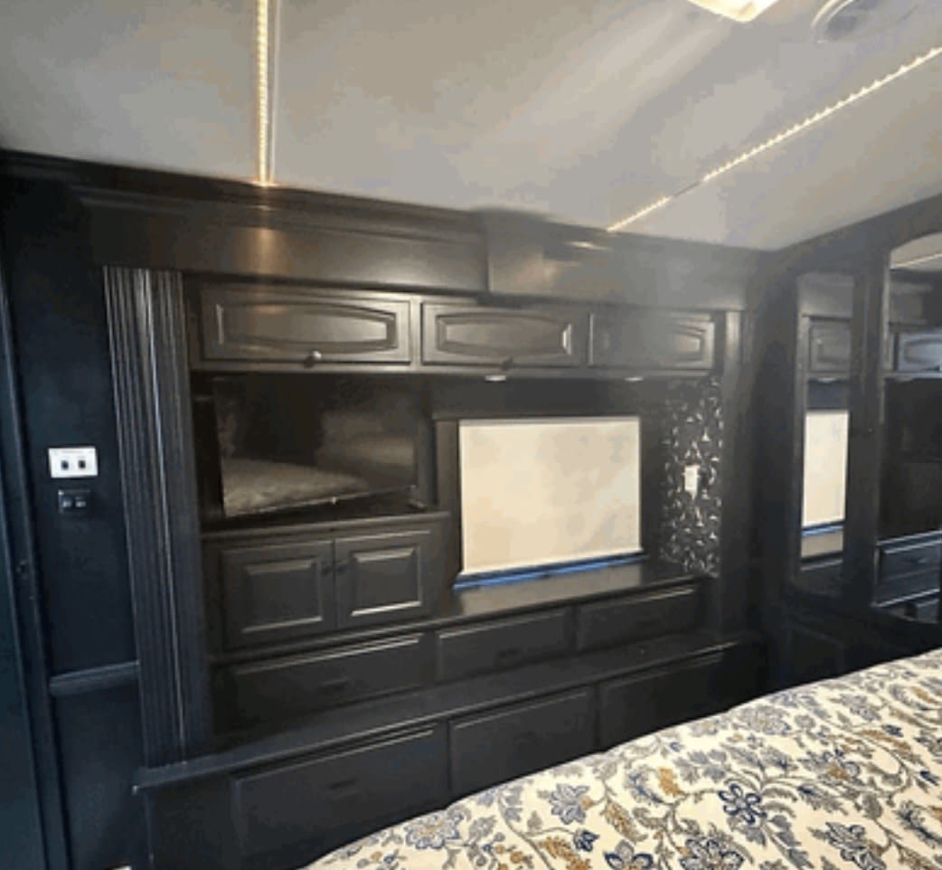 Cozy RV rental bedroom features dark built-in cabinetry, TV, storage, and ceiling LED lighting, seen over a patterned bed.. Newmar Dutch Star 2008