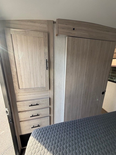 RV rental interior: A compact bedroom with light wood wardrobe, drawers, and a sliding door, beside a bed. Modern & functional.. Cruiser RV Shadow Cruiser 248RKS 2022