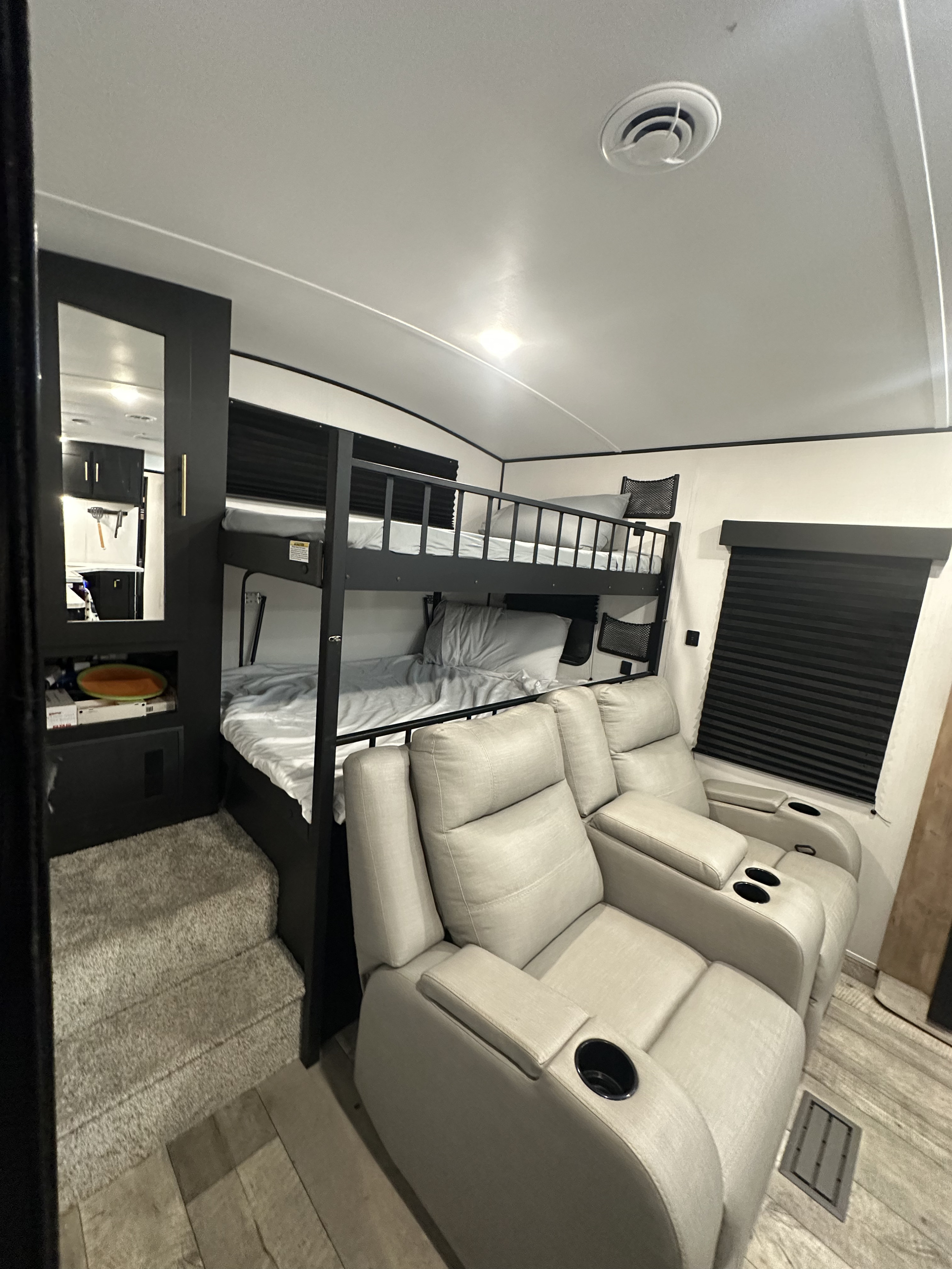 RV rental interior with comfy bunk beds, recliners with cup holders, and a staircase leading to a mirrored cabinet.. Keystone RV Springdale 2023