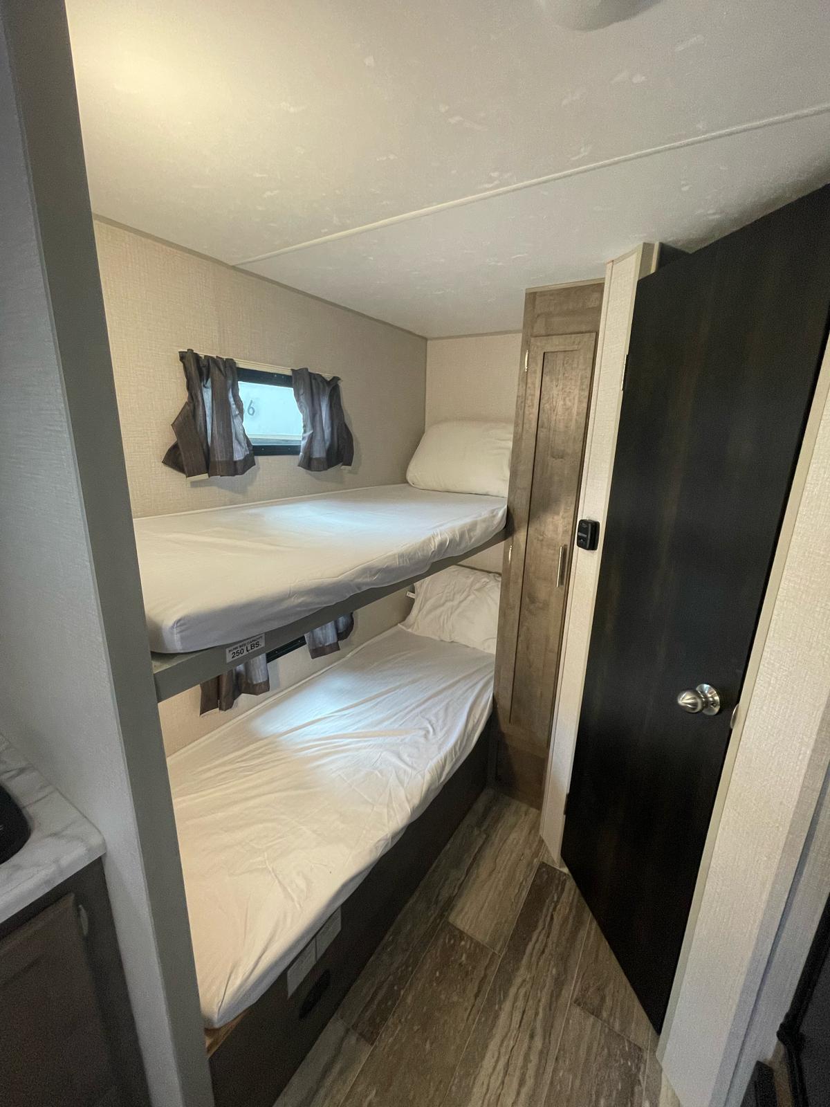 Inside an RV rental: two compact bunk beds with white linens, a window, and storage, perfect for small groups.. KZ Escape 2020