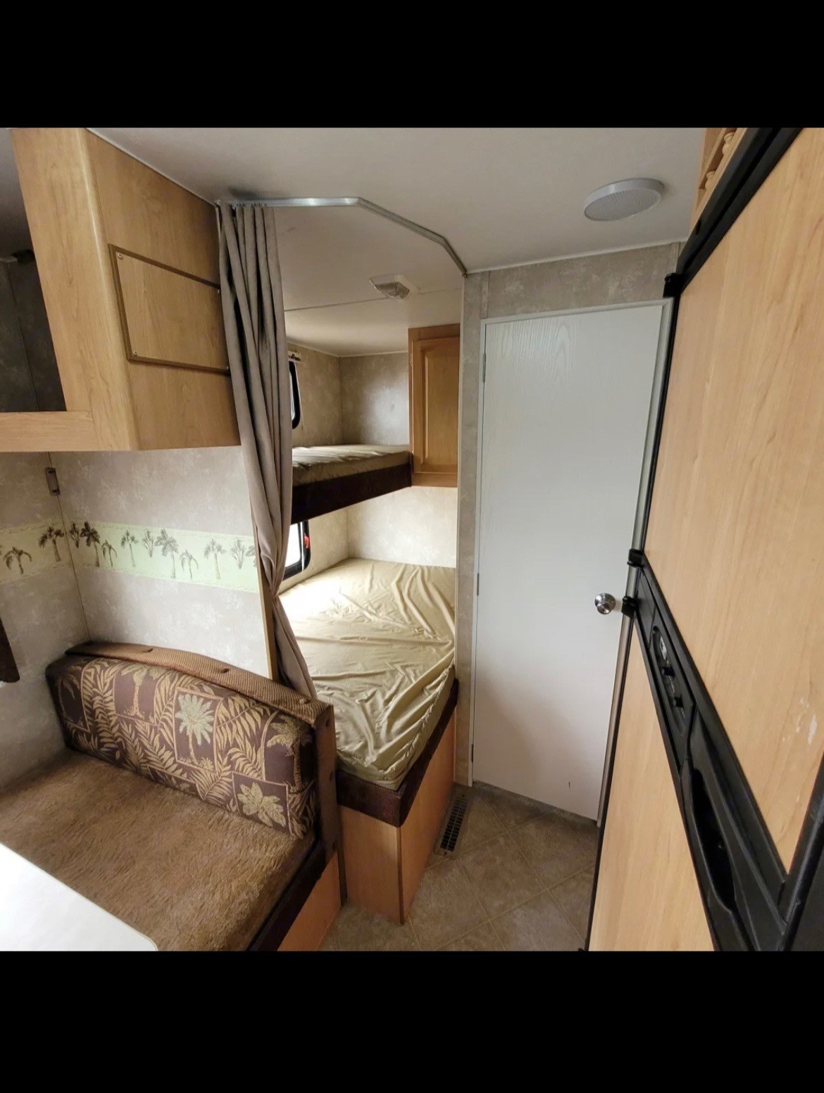 RV rental interior featuring cozy bunk beds with a privacy curtain, a patterned dinette, and a wood-paneled refrigerator.. Thor Wave 2006