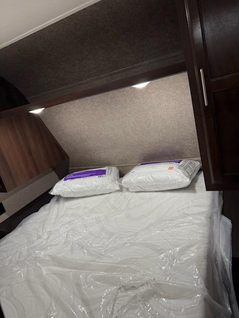 Cozy RV rental bedroom with a new, plastic-covered mattress and pillows, featuring built-in overhead lighting and storage.. Jayco Jay Flight SLX Baja Edition 2019