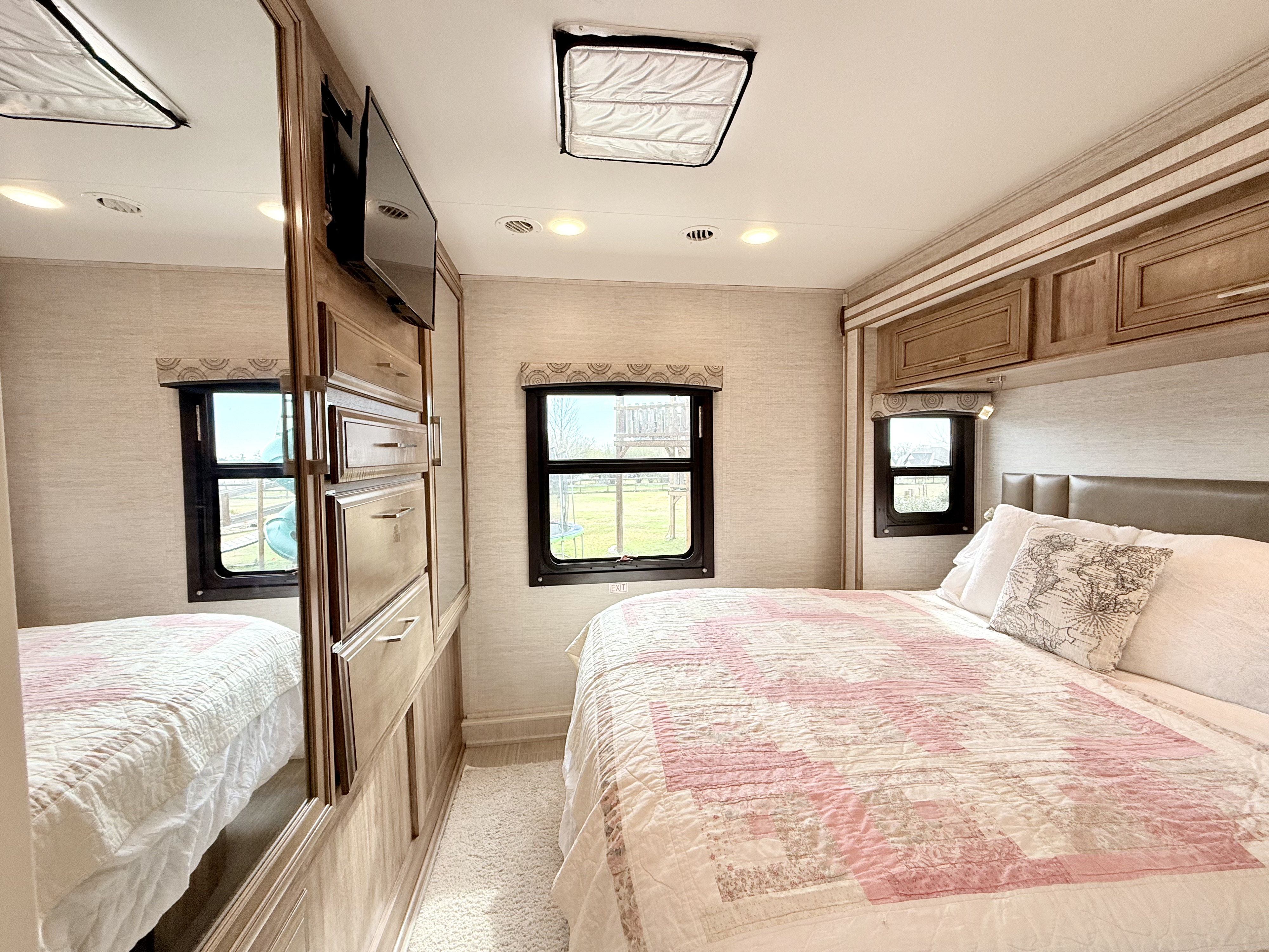 Comfortable RV rental bedroom featuring a bed with a pink quilt, built-in storage, and sunlit windows. Perfect for travel.. Entegra Coach Odyssey 2021