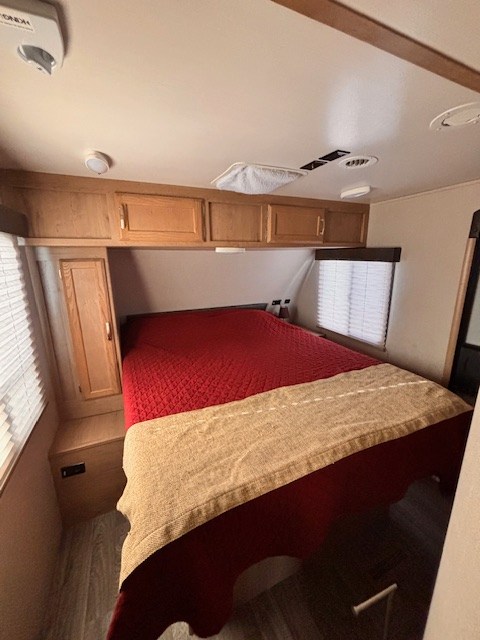 Inside an RV rental: a comfortable bedroom with overhead cabinets, cozy red bedding, and blinds.. Winnebago 2401RG 2020