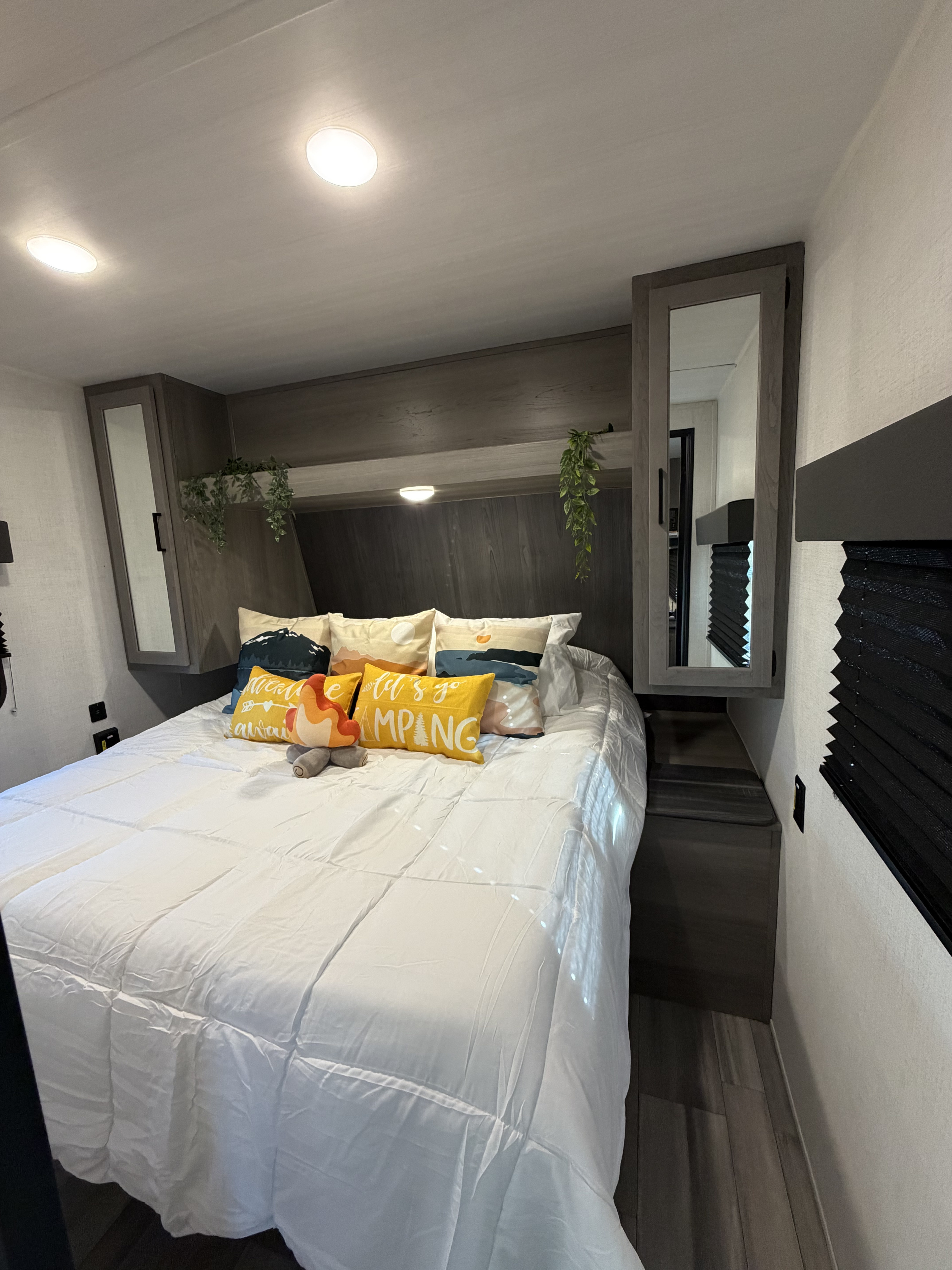 Cozy RV rental bedroom with a comfy bed, camping-themed pillows, overhead storage, and integrated mirrors.. Keystone RV Hideout 2024