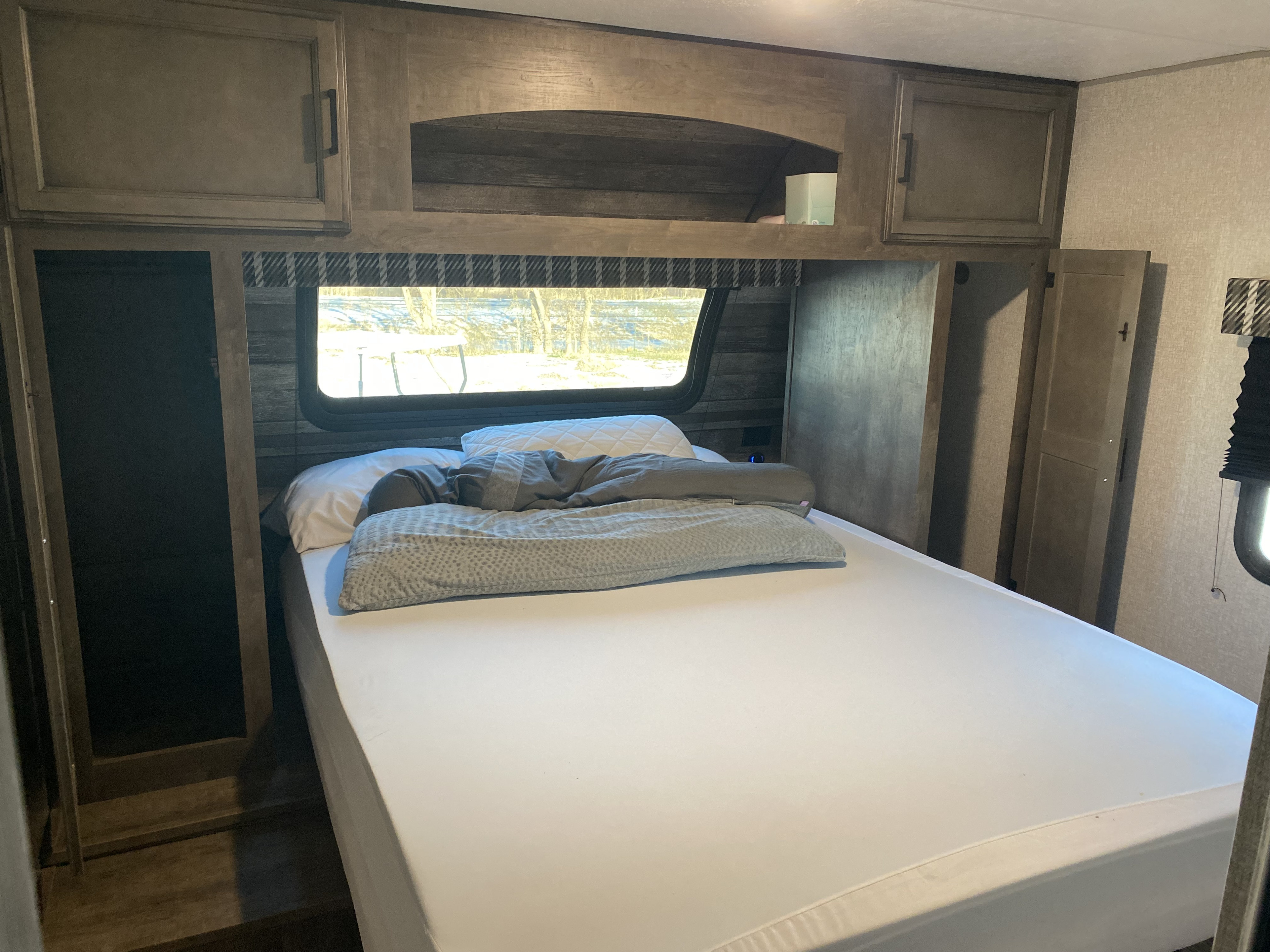 RV rental bedroom featuring a cozy bed, overhead cabinets, and a window. Ideal for a comfortable camper stay.. Venture Stratus 2022