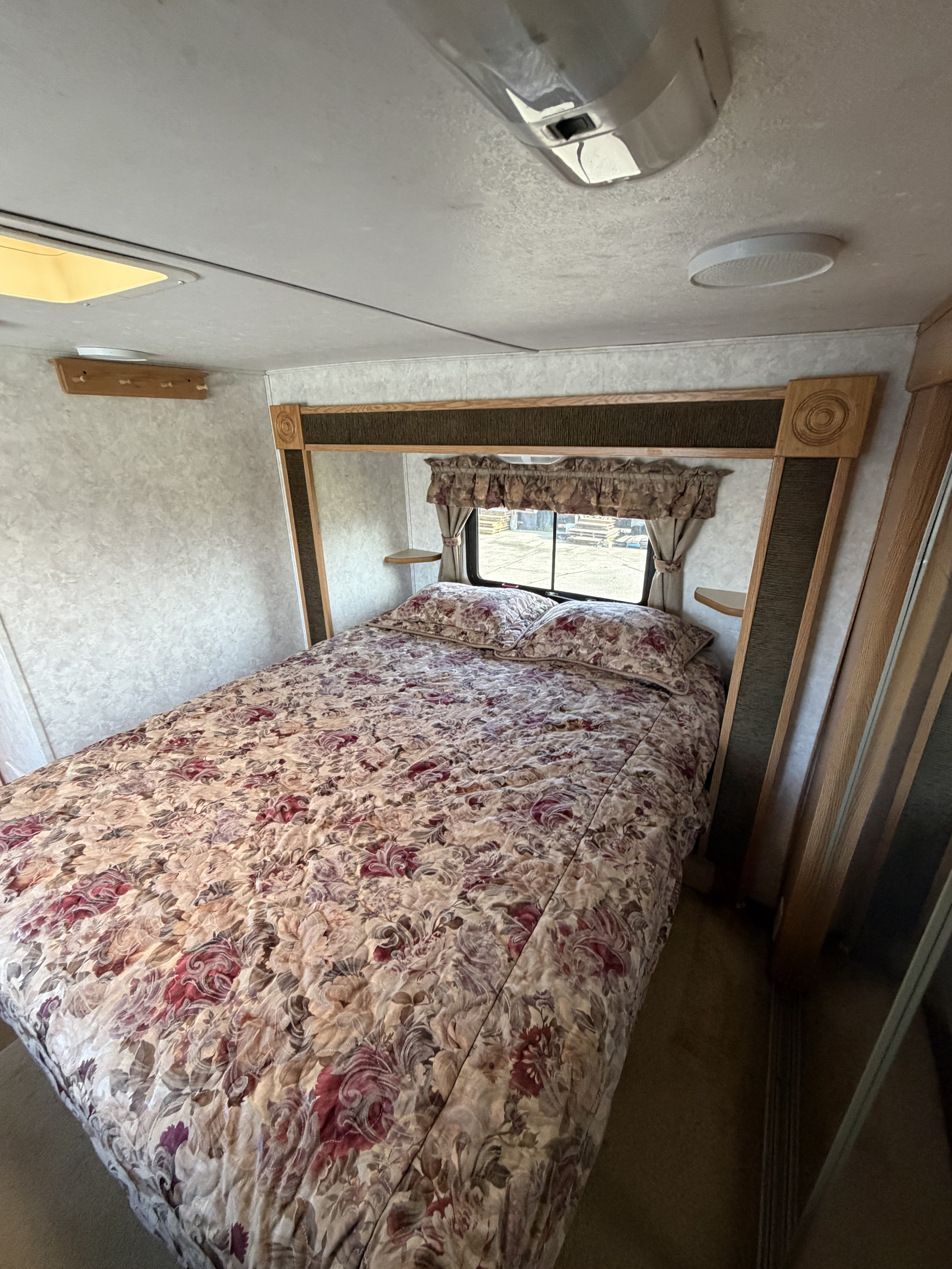 RV rental bedroom featuring a floral patterned bed, window, wooden headboard with shelves, and ceiling lights.. Keystone RV Montana Mountaineer 2004