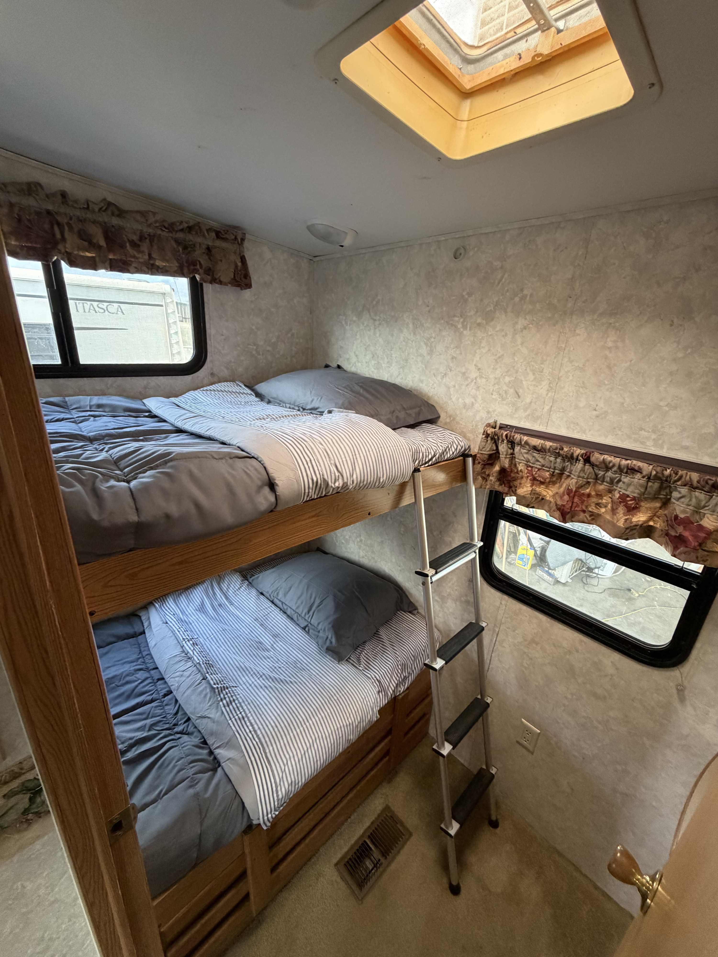 Bright RV rental bunkhouse featuring two bunk beds with grey bedding, a ladder, a window, and an overhead skylight.. Keystone RV Montana Mountaineer 2004