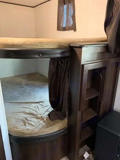RV rental interior featuring bunk beds: a lower bunk with privacy curtain and an adjacent storage unit with shelves.. Jayco Jay Flight SLX Baja Edition 2018