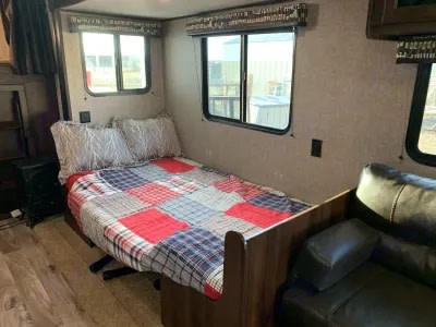Inside an RV rental: A comfy bed with a colorful patchwork quilt, a black leather sofa, and bright windows.. Jayco Jay Flight SLX Baja Edition 2018