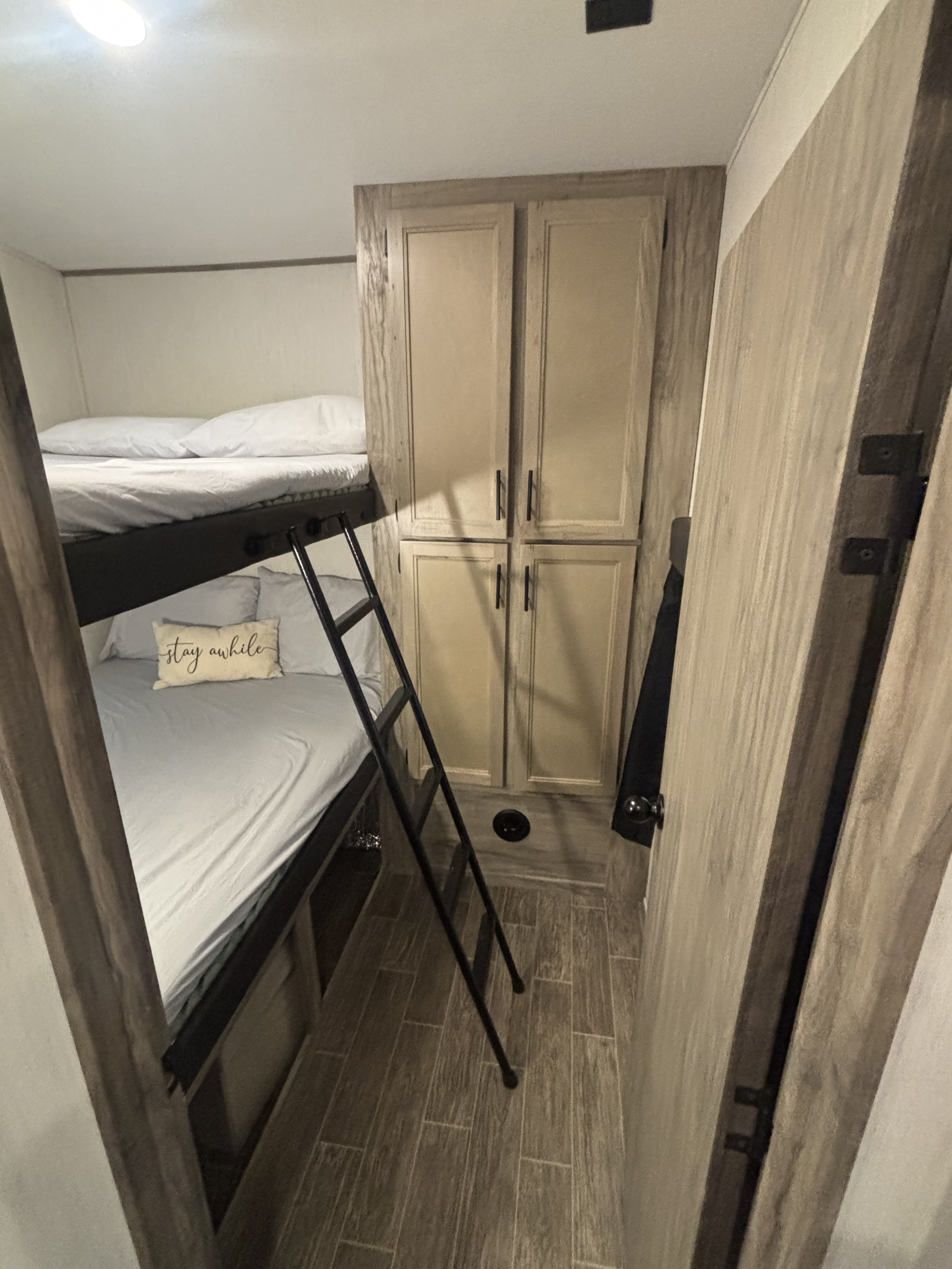 Cozy rv rental interior features bunk beds with a ladder, storage cabinets, and wood-look flooring. "Stay awhile" pillow visible.. Forest River Cherokee Arctic Wolf 2022