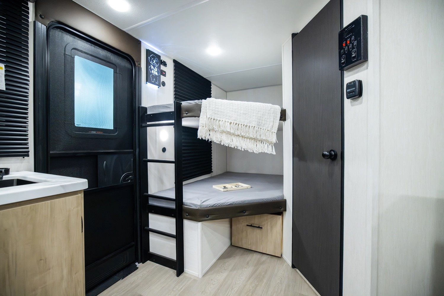 Inside a compact RV rental, showcasing cozy bunk beds, an entrance door, and utility controls for comfortable travel.. Forest River Campsite Reserve 17LS 2026