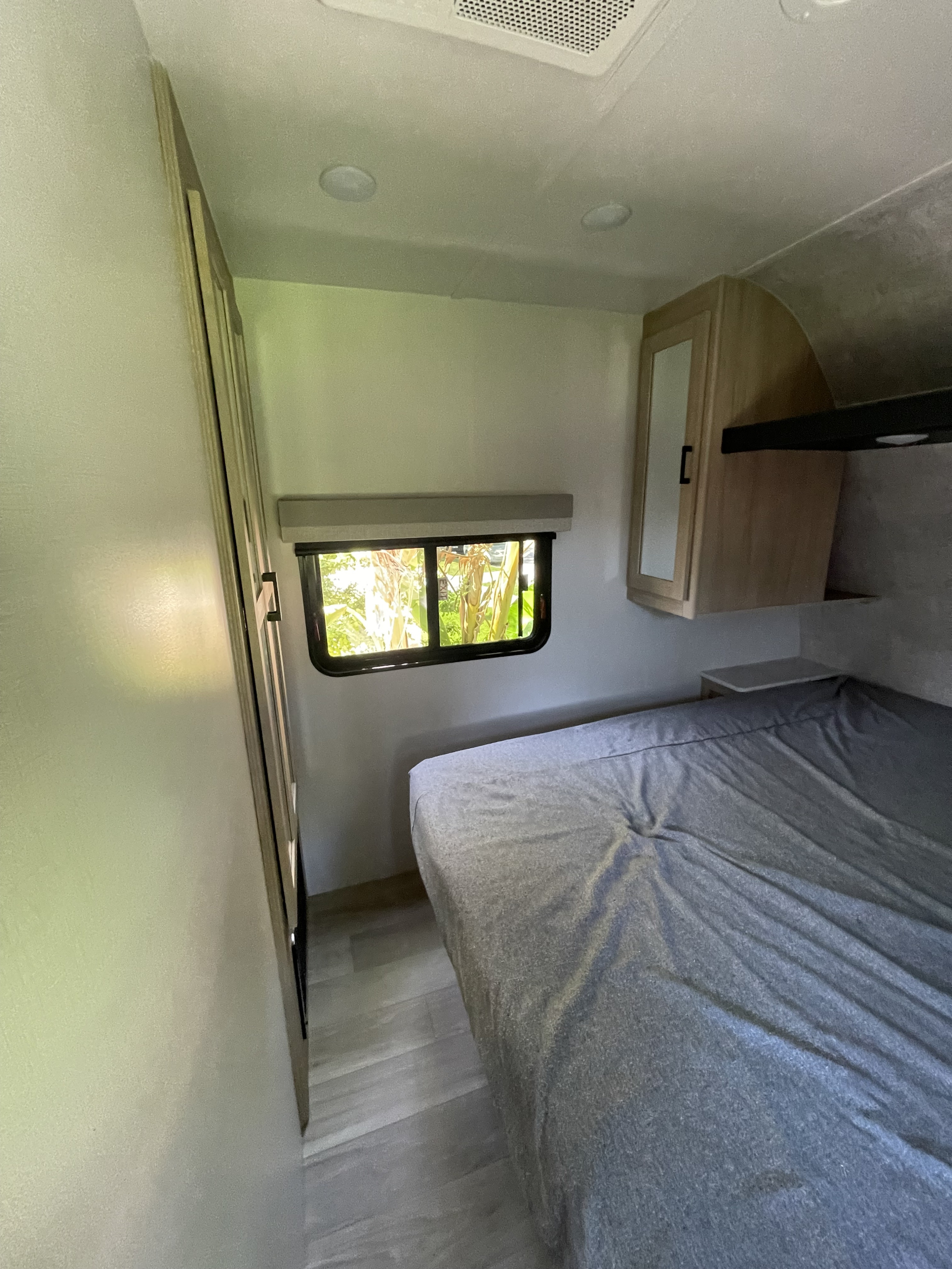 Cozy RV rental bedroom interior with a grey bed, window, wardrobe, and overhead cabinets.. Winnebago Voyage 2023