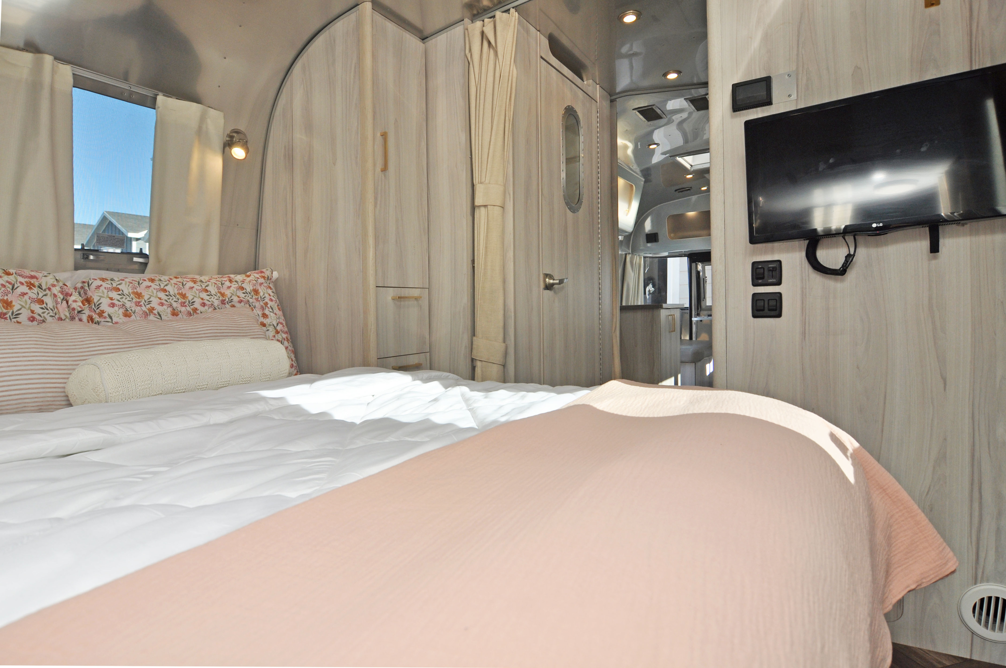Cozy bedroom inside a modern rv rental with floral pillows, TV, and light wood interior. Perfect for travel and relaxation.. Airstream International 2021