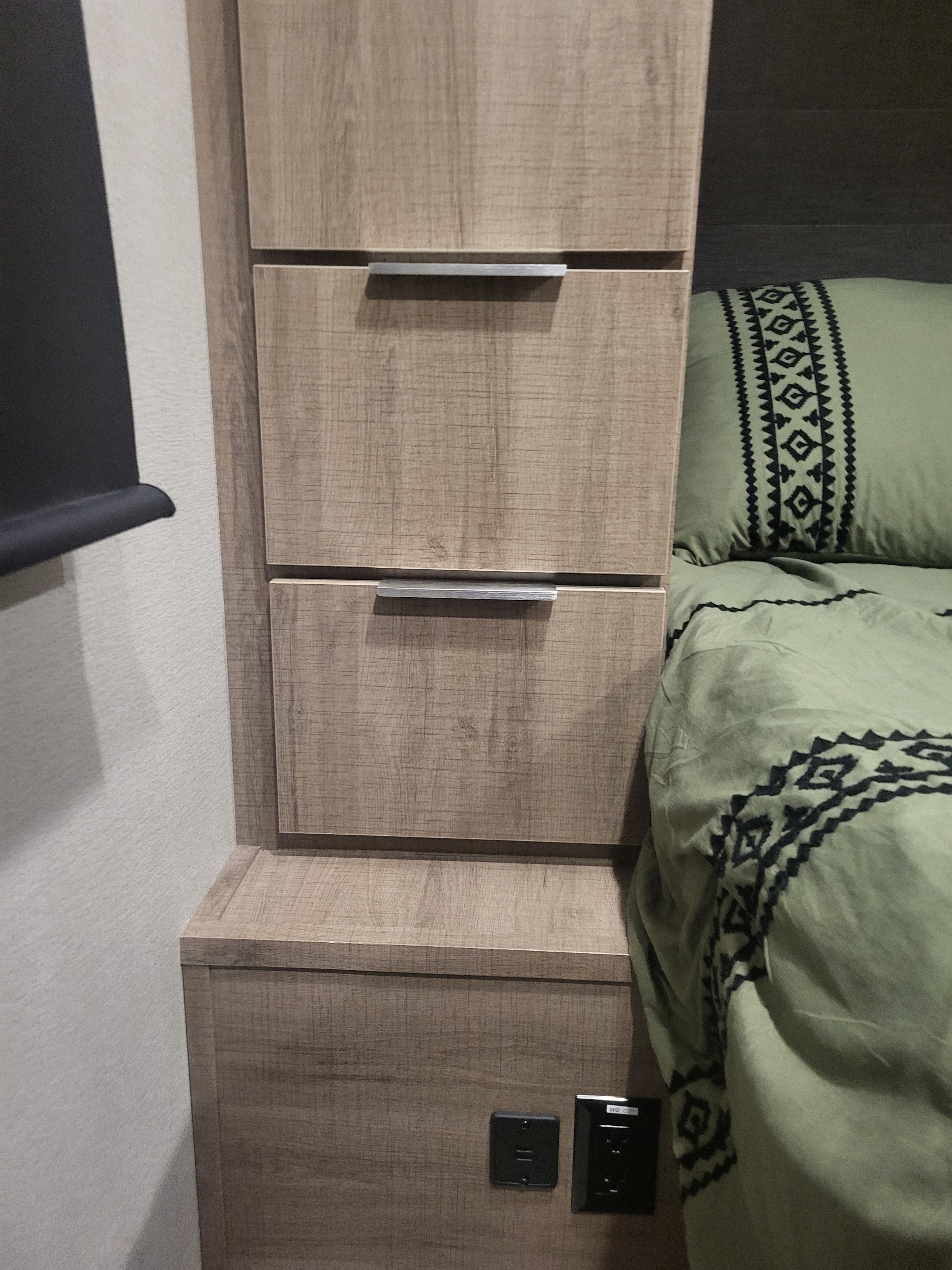 Modern RV rental bedroom features wood-look drawers, comfy patterned bedding, and convenient charging outlets.. Grand Design Imagine 2020