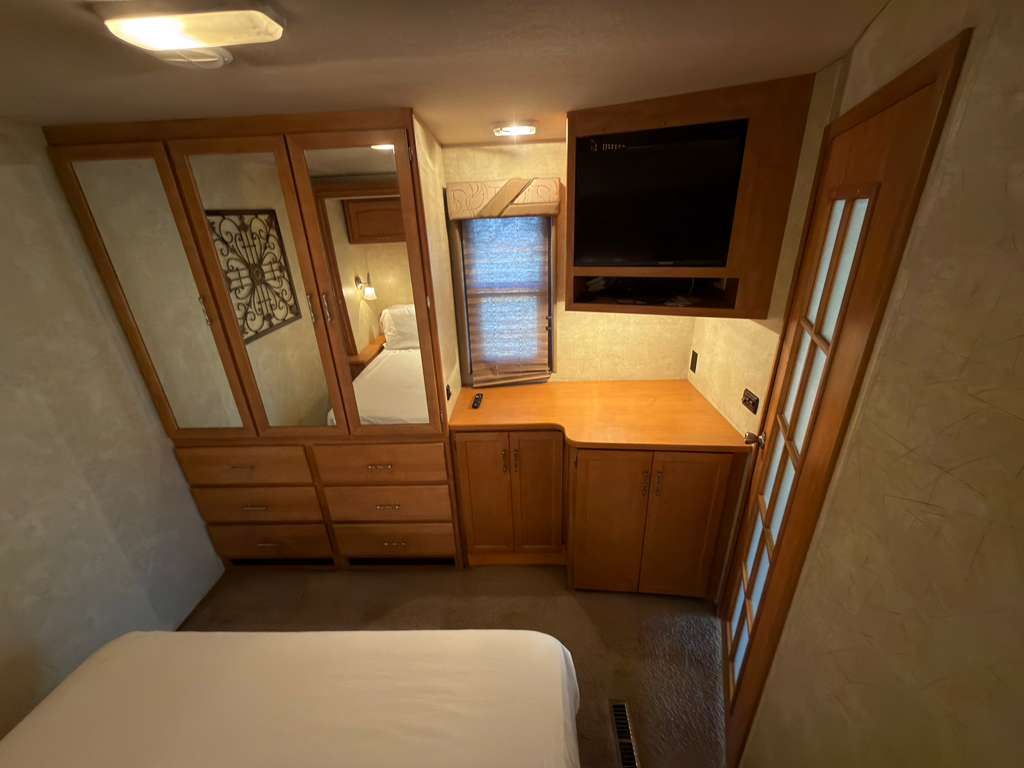 RV rental bedroom featuring a built-in TV, large mirrored wardrobe, storage cabinets, and a cozy bed for your travels.. Winnebago Voyage 2008