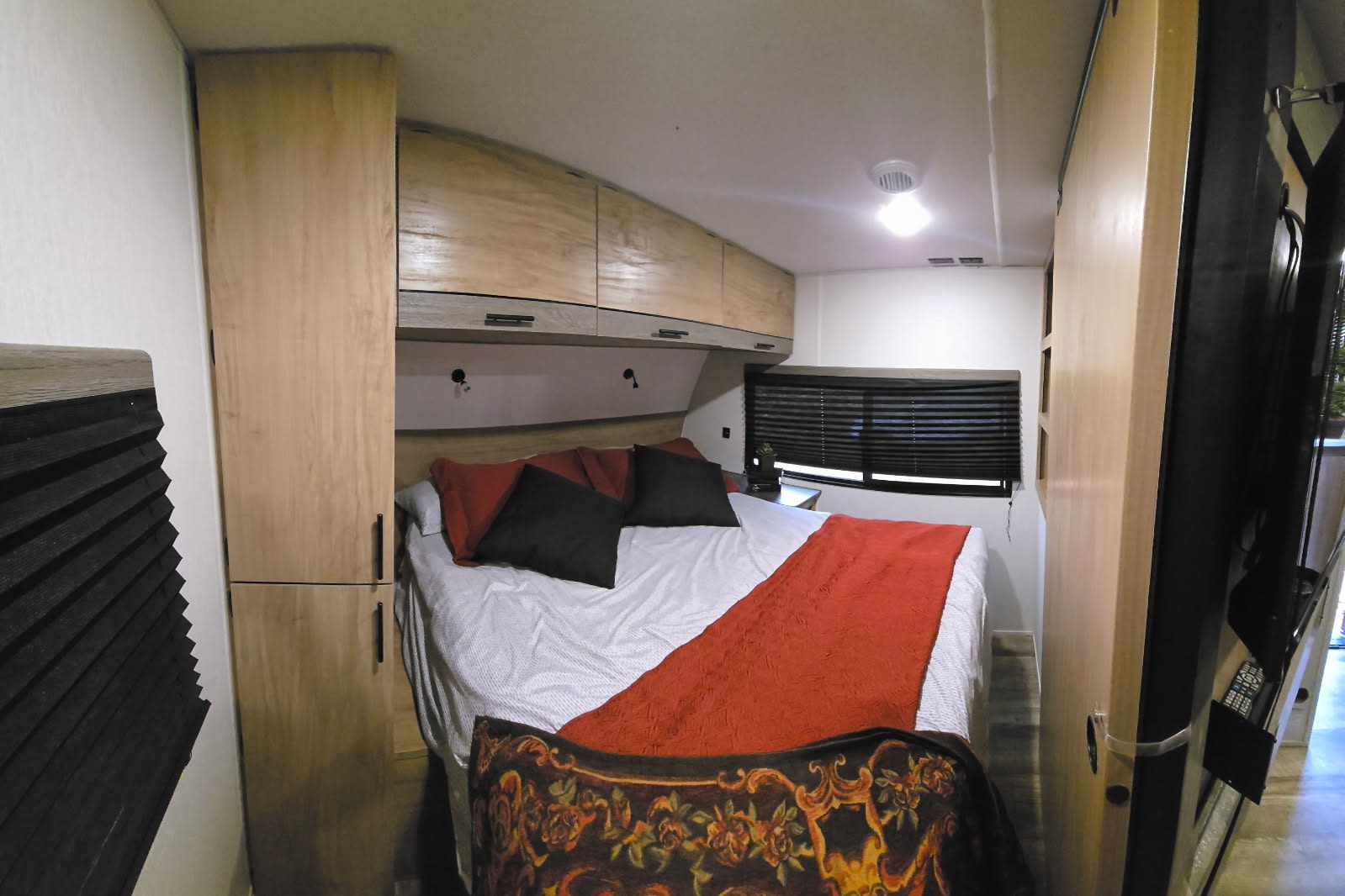 Spacious rv rental bedroom with a bed, overhead and side cabinets, window blinds, and a TV. Ready for your next adventure.. Forest River Campsite Reserve 2024
