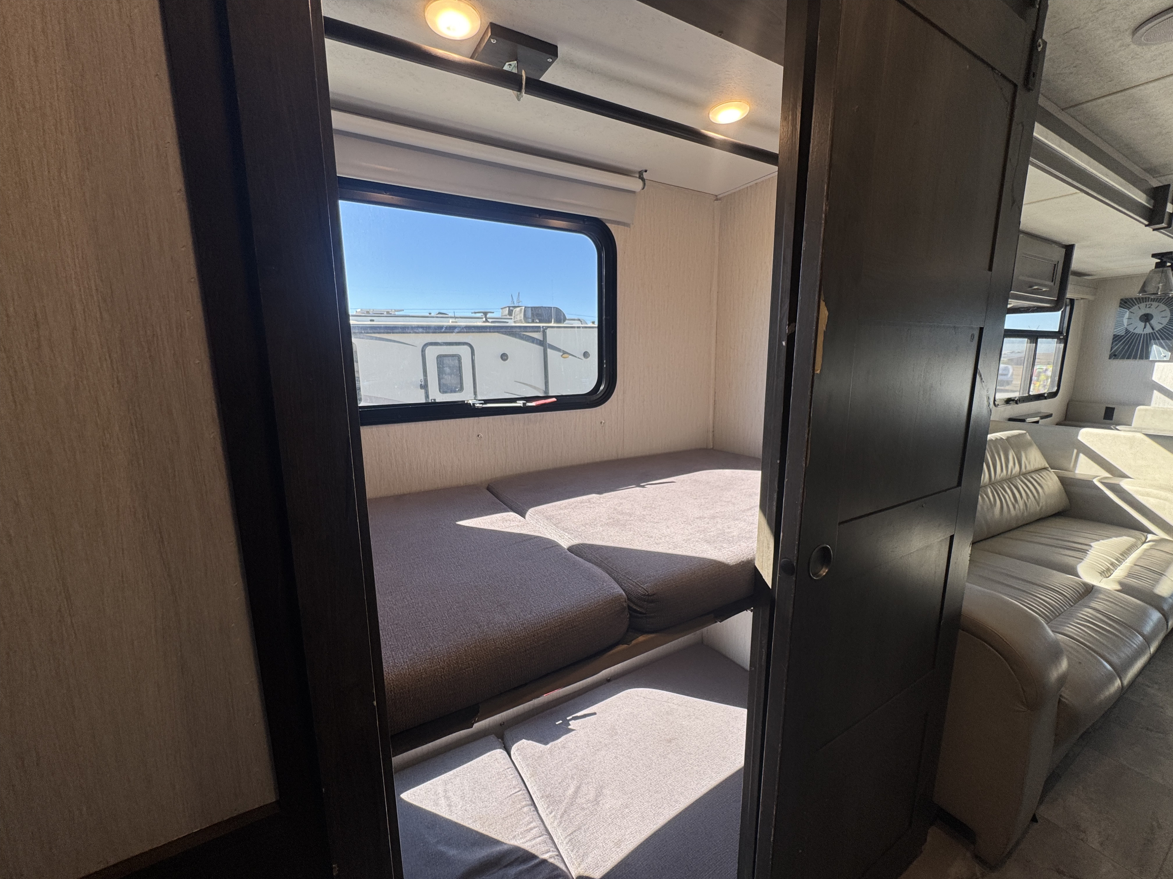 RV rental interior featuring cozy bunk beds by a window, with a light-colored sofa visible in the adjacent living area.. Forest River Coachmen Encore 2022