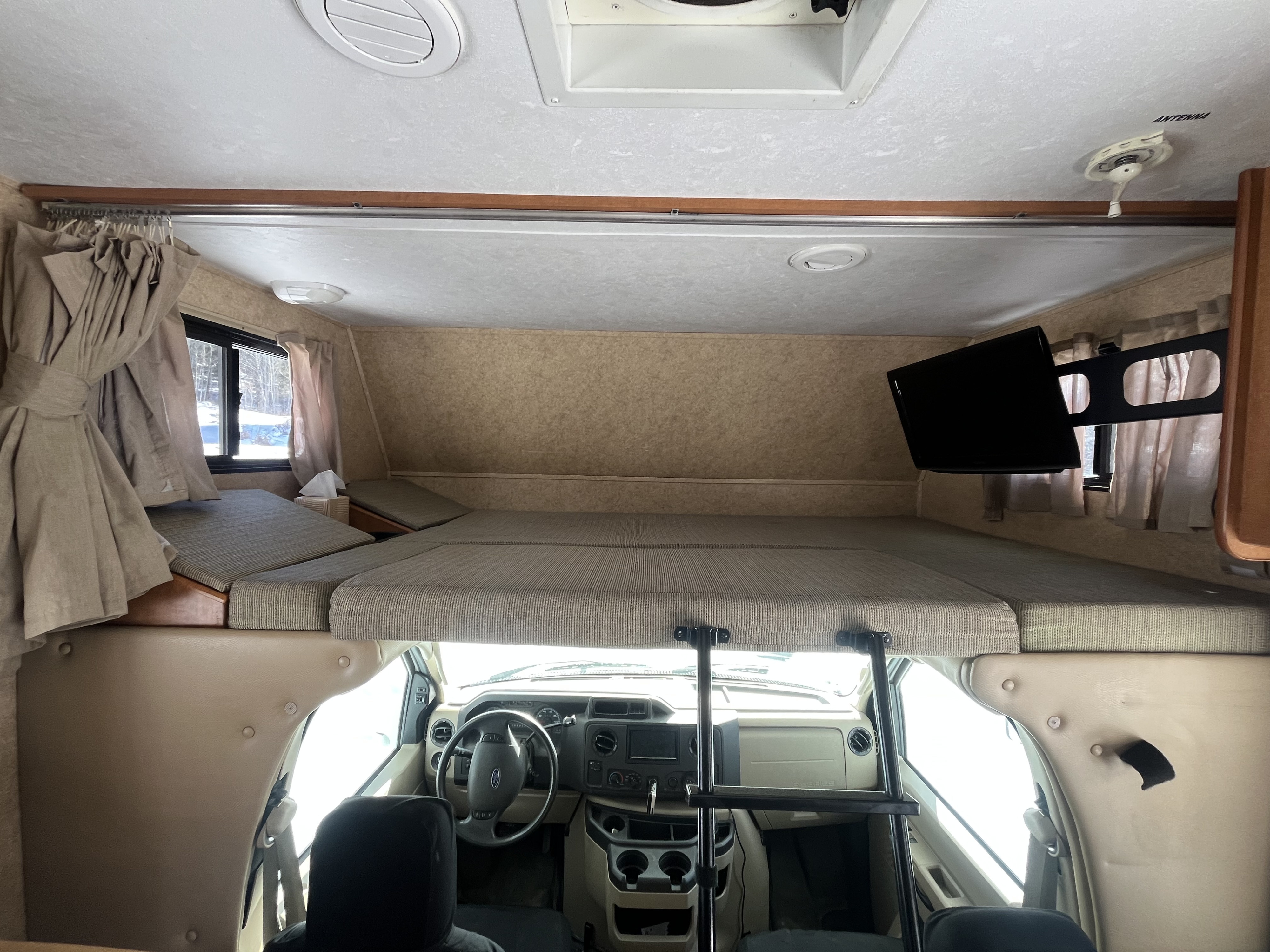 RV rental interior: A spacious over-cab bunk bed, driver's cockpit, and TV setup for comfortable trips.. Forest River Sunseeker 2012