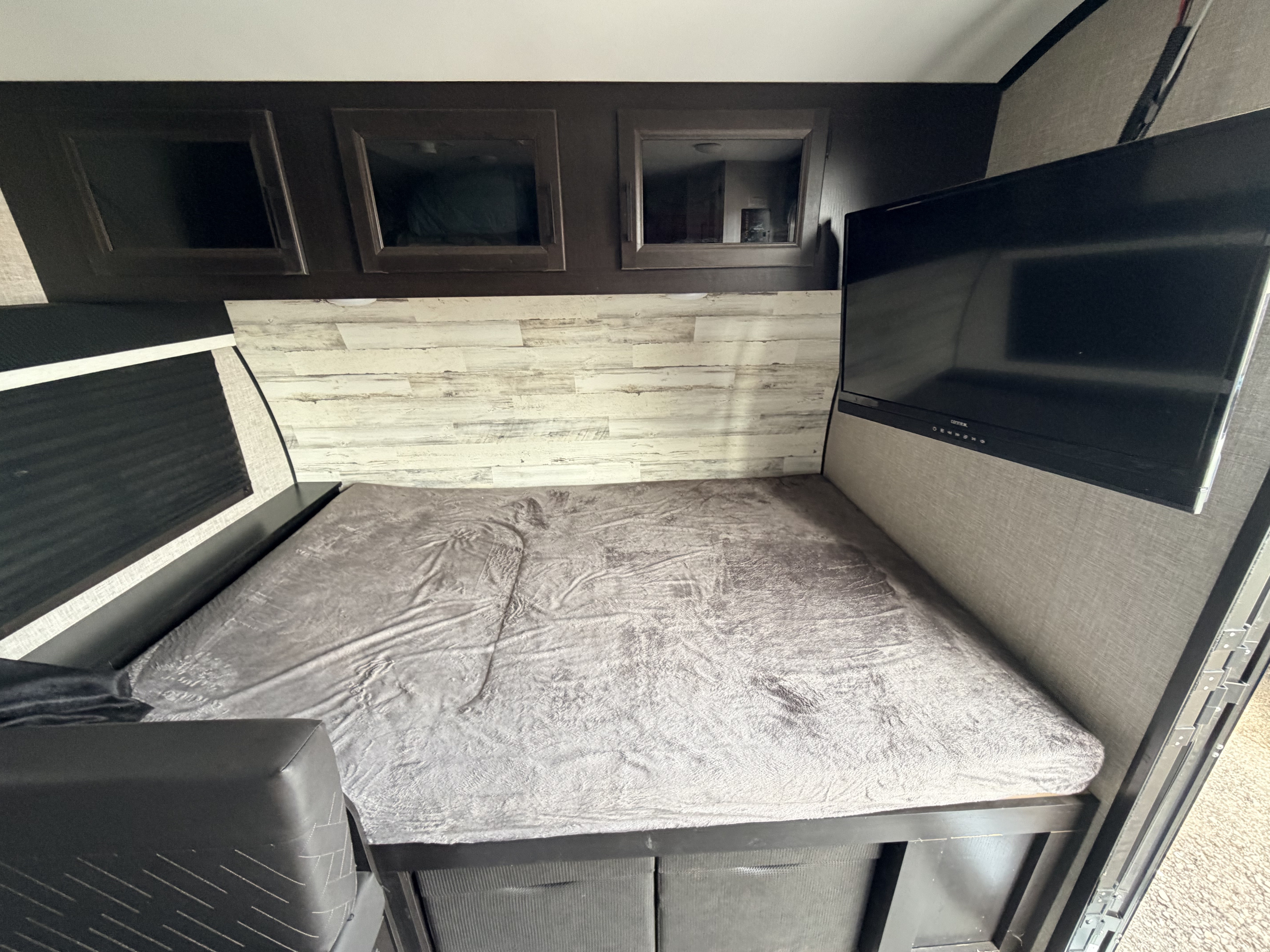 Cozy RV rental sleeping area featuring a comfy bed, wood-paneled wall, wall-mounted TV, and overhead cabinets.. Jayco Jay Feather Micro 2022