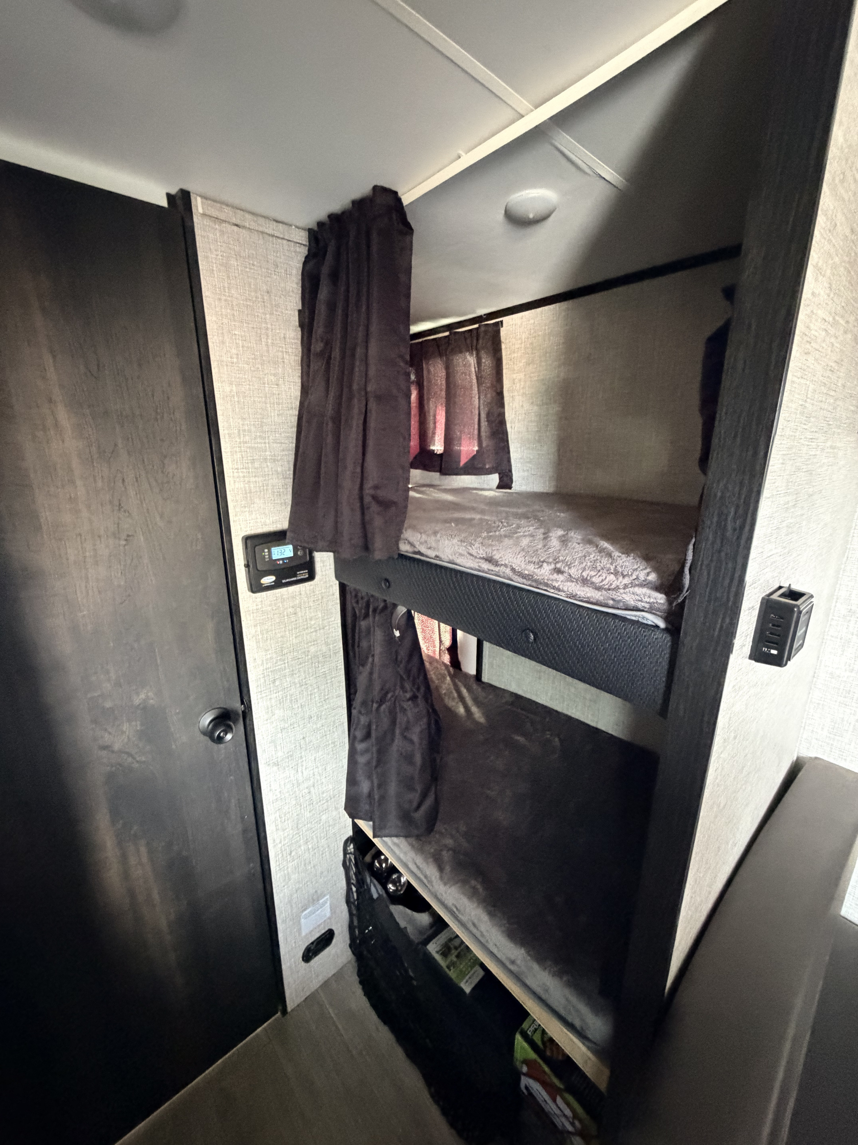 Compact rv rental bunk beds feature dark privacy curtains, plush grey bedding, a control panel, and USB charging ports.. Jayco Jay Feather Micro 2022
