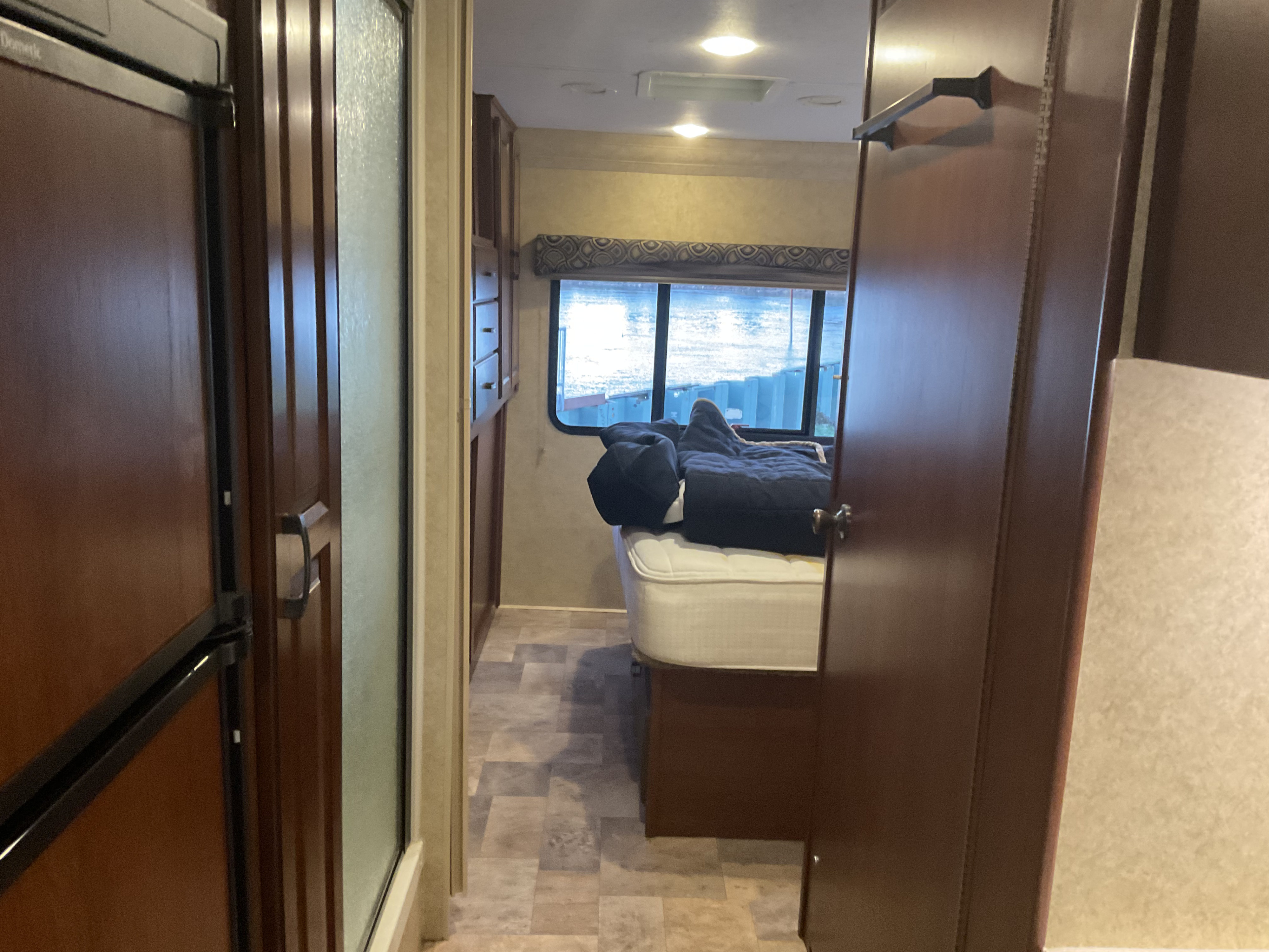 RV rental interior: Hallway leads past the fridge and shower to a bedroom with a bed and window view of the water.. Forest River Sunseeker 2014