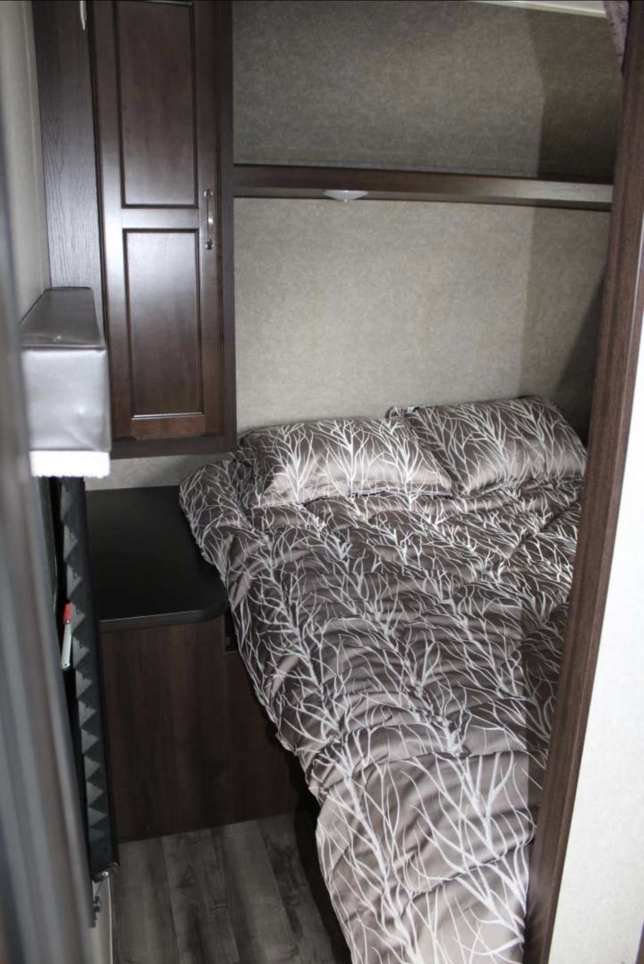 Cozy RV rental bedroom with patterned bed, dark wood cabinet, and storage shelf.. Jayco Jay Flight SLX 2018