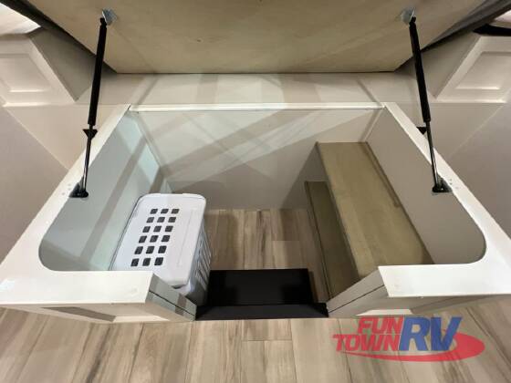 RV rental storage: Spacious under-bed compartment revealed by gas struts, holding a laundry basket and wooden platform.. Brinkley RV Model I 2025