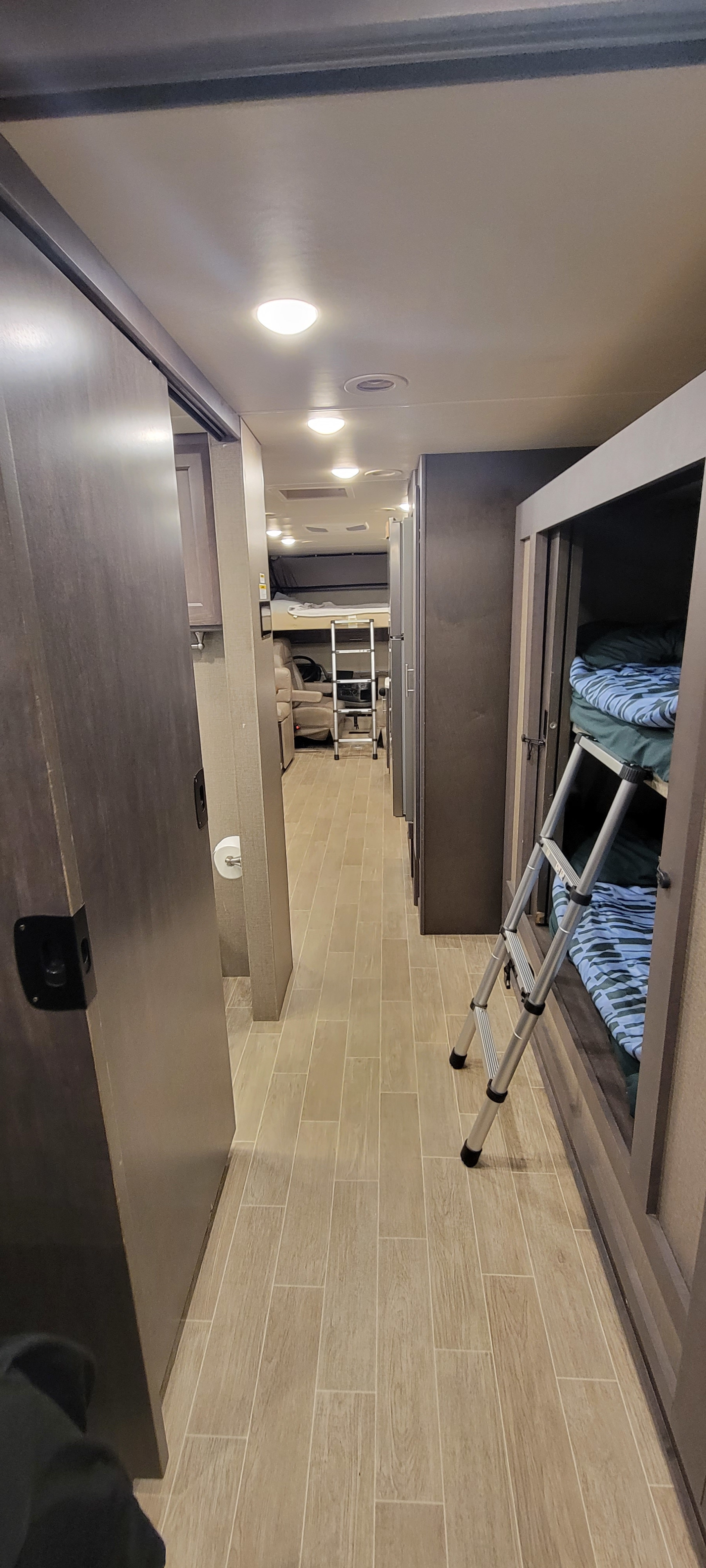 Inside an rv rental: a well-lit hallway with bunk beds on the right, leading to the front seating and cab-over bed.. Thor Miramar 2022