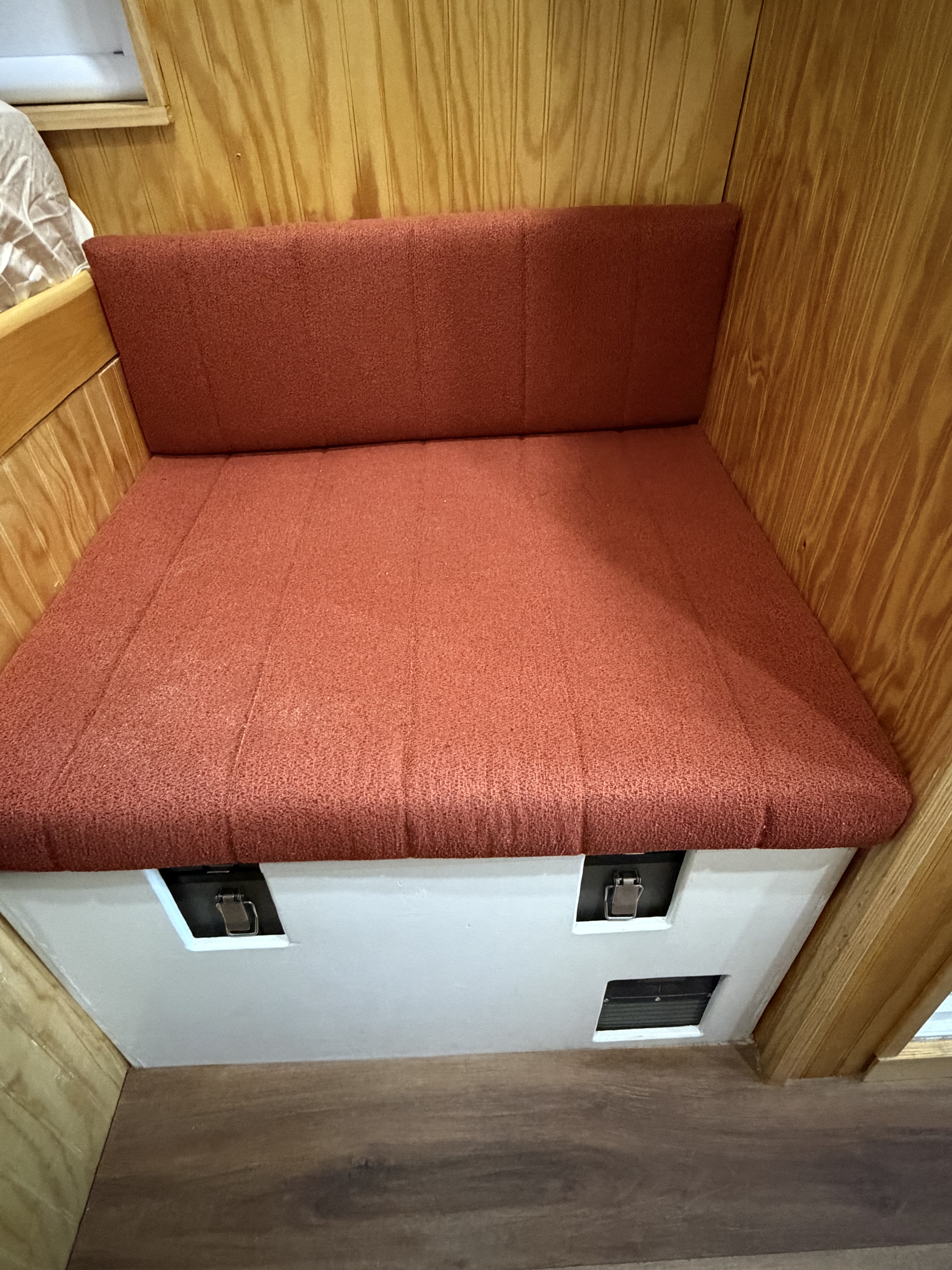 Cozy orange cushioned bench and backrest in an rv rental, featuring wood paneling & under-seat storage with latches.. Dodge Ram 2500 2024