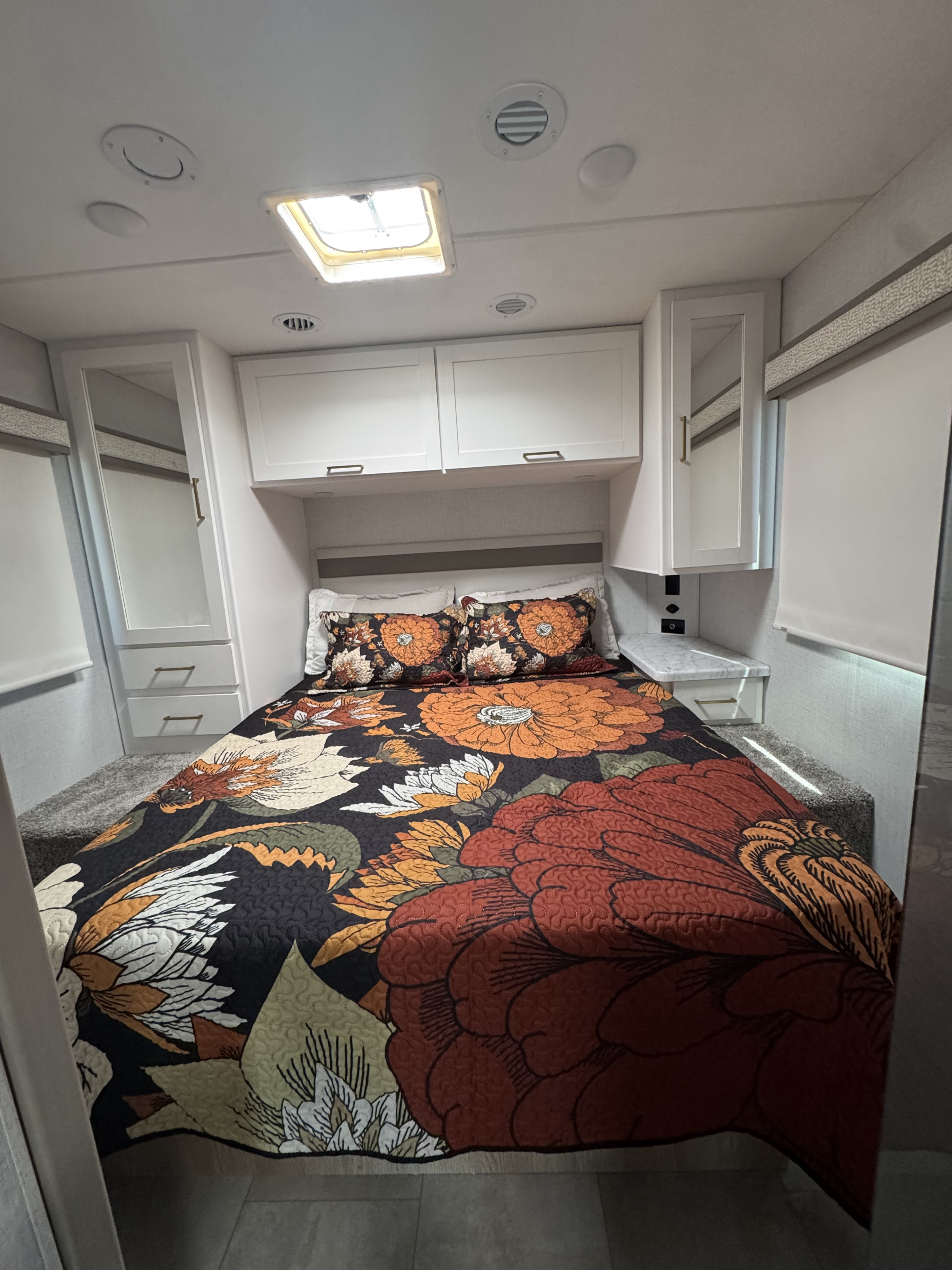 Cozy RV rental bedroom featuring a vibrant floral quilt, ample overhead storage, and natural light from the skylight.. 1FDXE4FN7TDD10505 Thor Chateau 2026