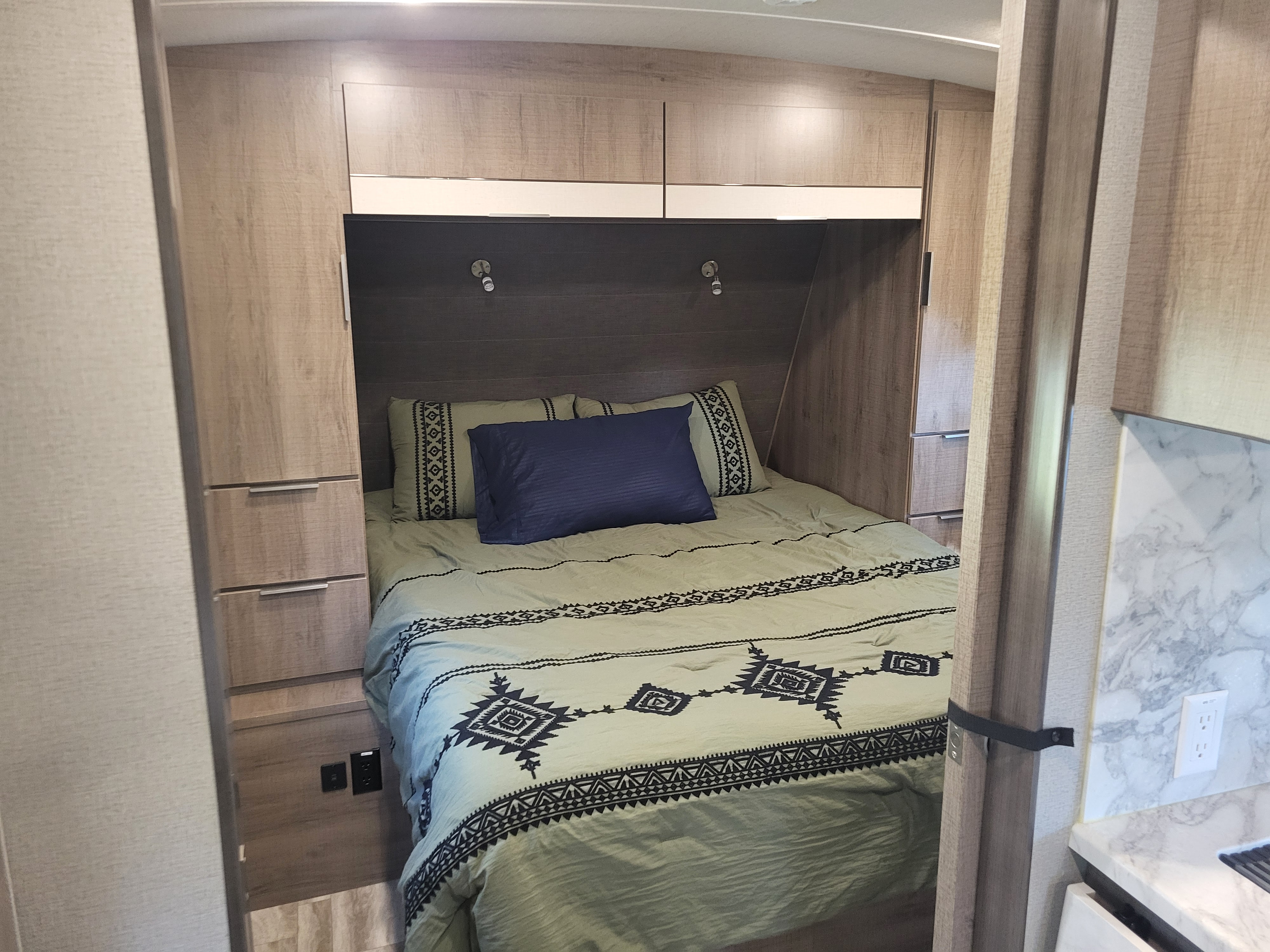 Cozy RV rental bedroom with patterned green bedding, built-in storage, and reading lights. A compact, functional RV interior.. Grand Design Imagine 2020