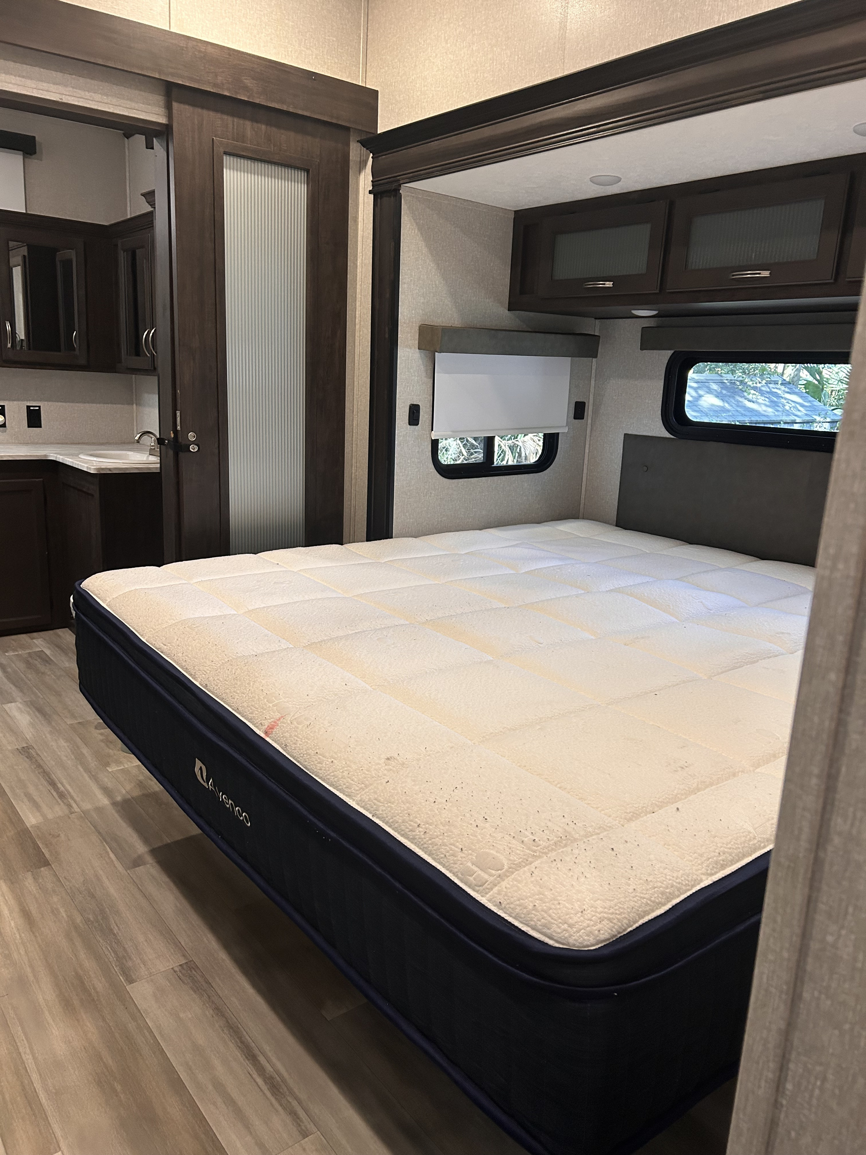 RV rental bedroom featuring a mattress, overhead storage, wood-look flooring, and a sliding door, with a glimpse of a sink area.. Coachmen 2021