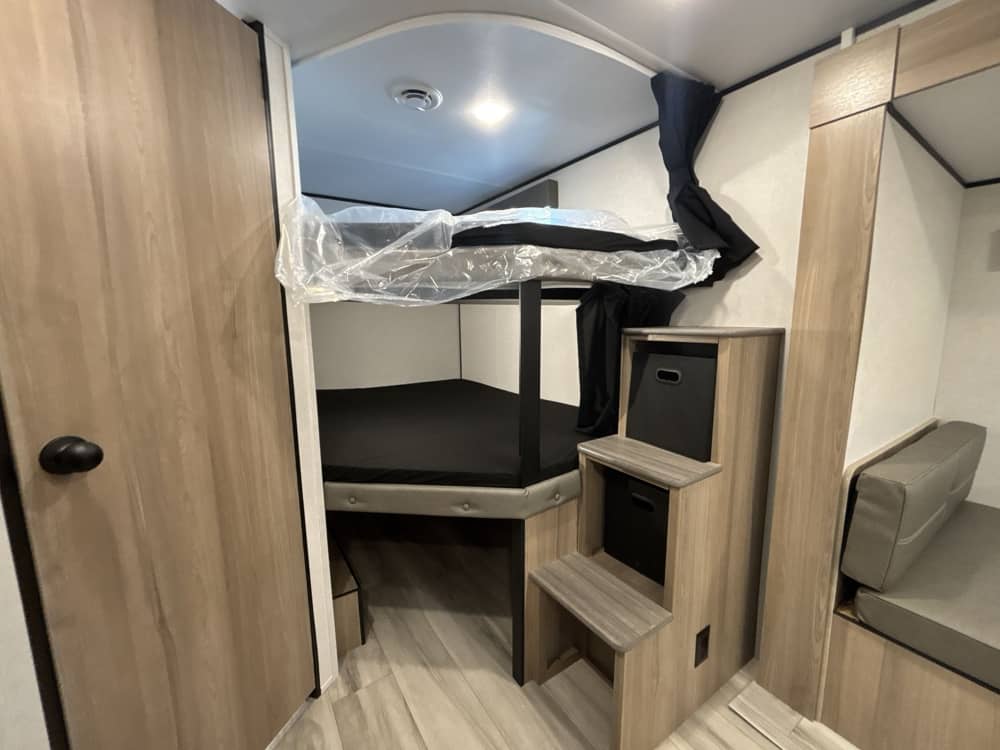 Cozy RV rental interior with bunk beds, an integrated storage-stair unit, and a small dinette, ideal for family trips.. Keystone RV Coleman Light 2025
