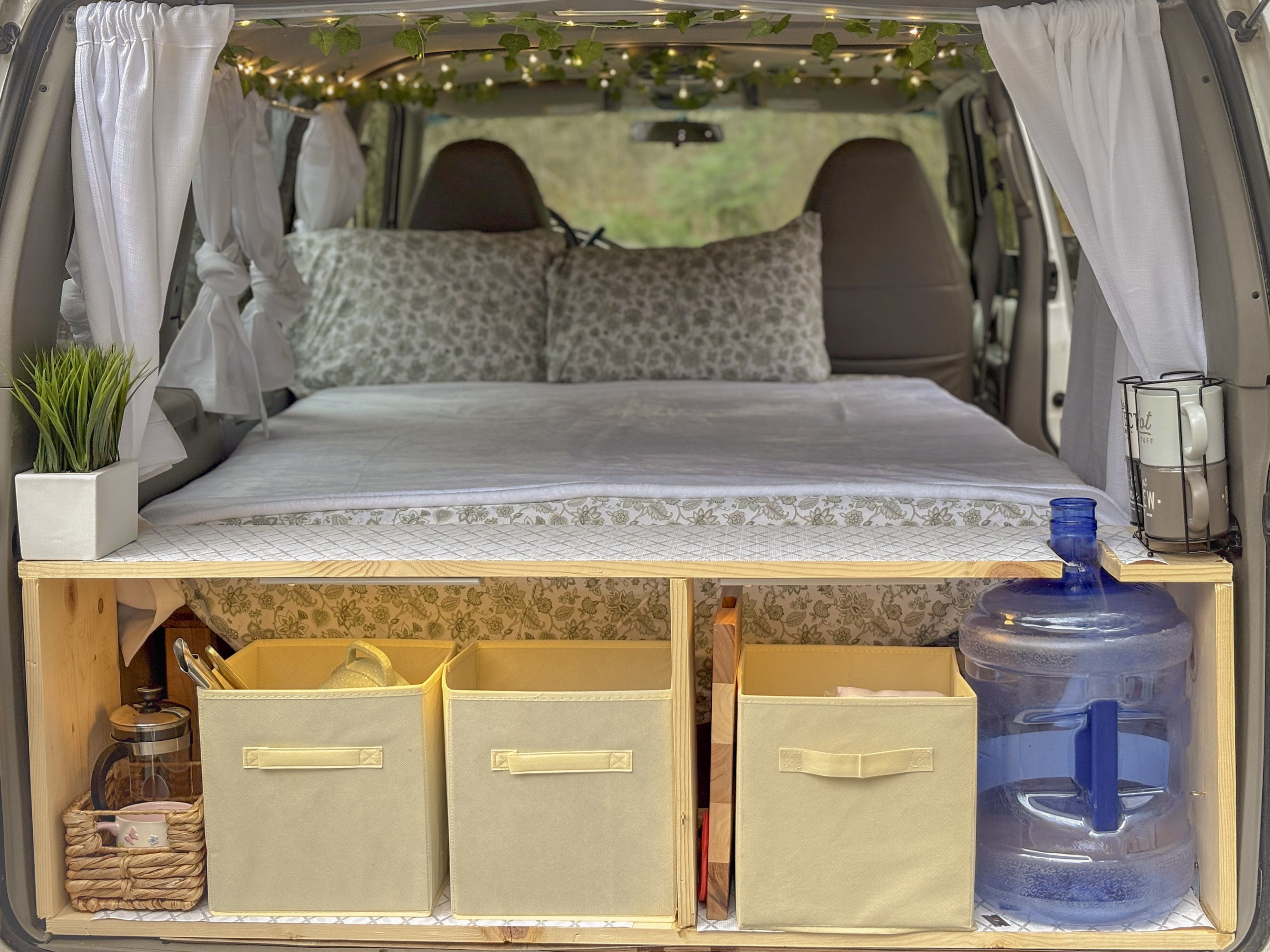 Cozy camper van rental interior: bed with patterned pillows, wood storage for bins, water jug, and fairy lights.. Chevrolet astro 2000