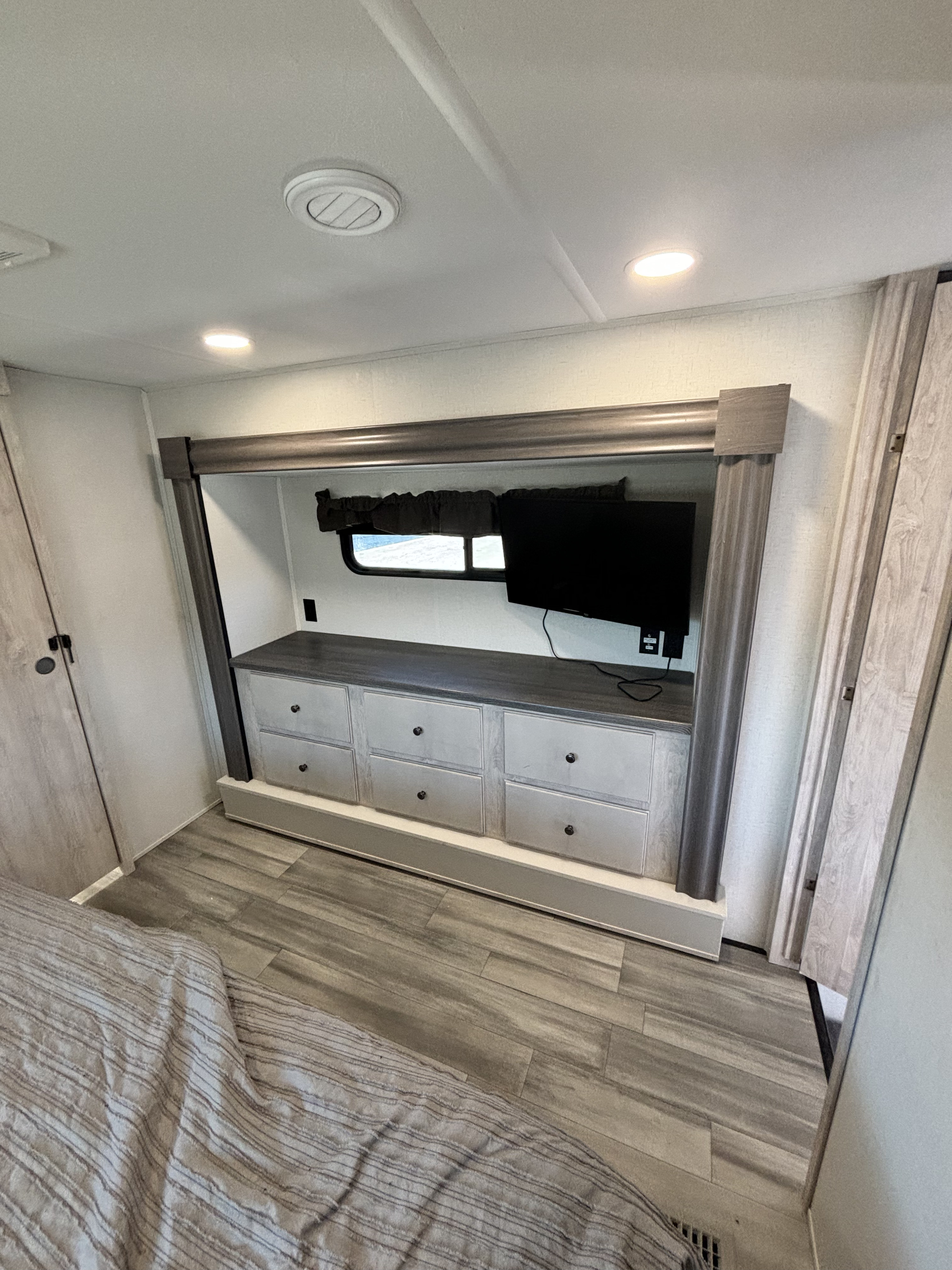 Modern RV rental bedroom featuring a built-in entertainment and storage unit with TV, drawers, and wood-look flooring.. Forest River Sierra 2024