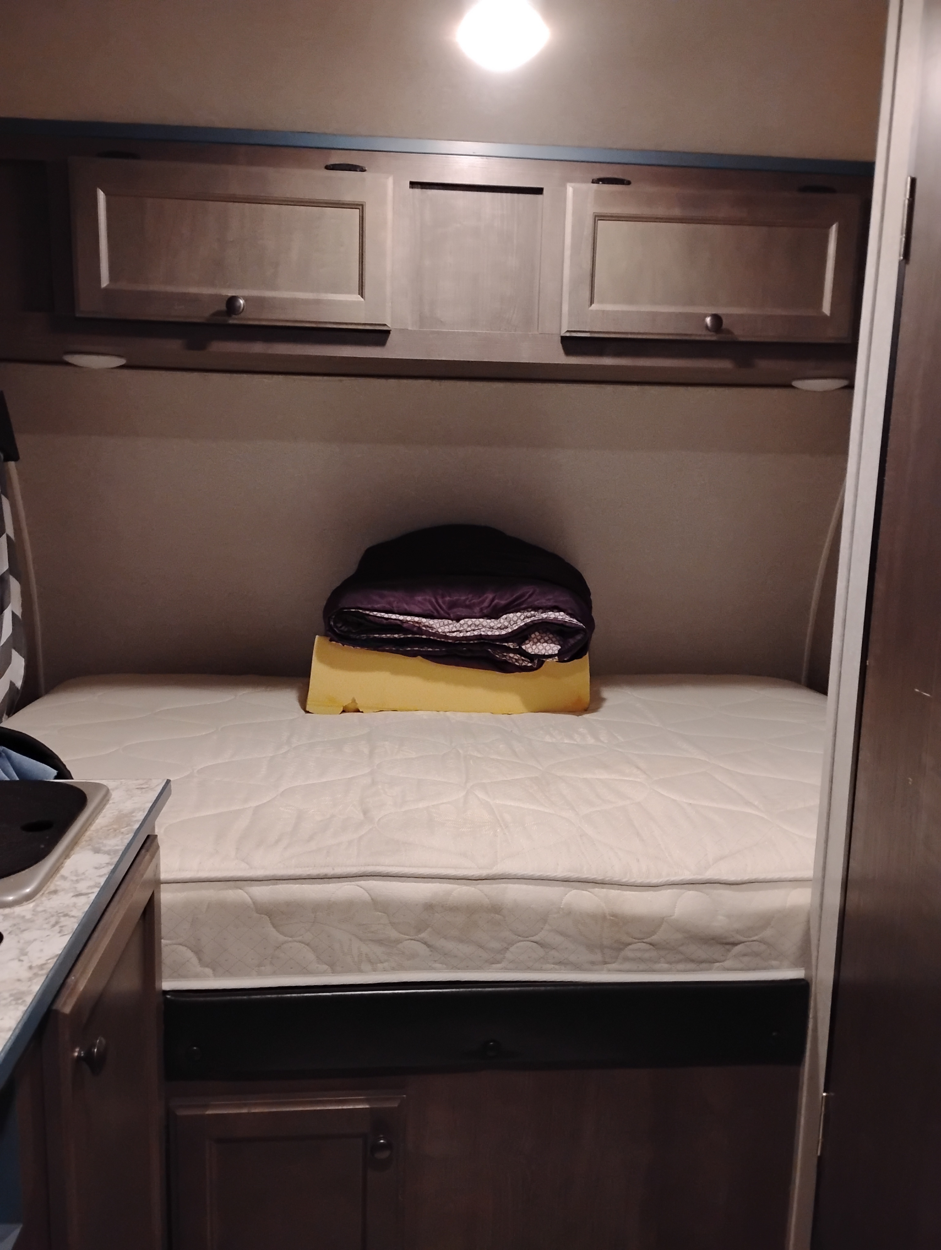 Cozy RV rental bedroom with a white mattress, overhead cabinets, warm lighting, and a folded blanket on a yellow foam support.. Sunray Sport 149 2021