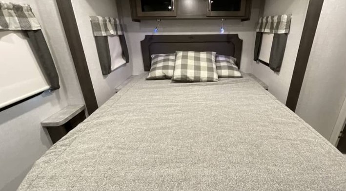 Cozy RV rental bedroom: large bed with plaid pillows, storage cabinets, and side windows. Perfect for road trips.. Keystone RV Flagstaff Super Lite 2023