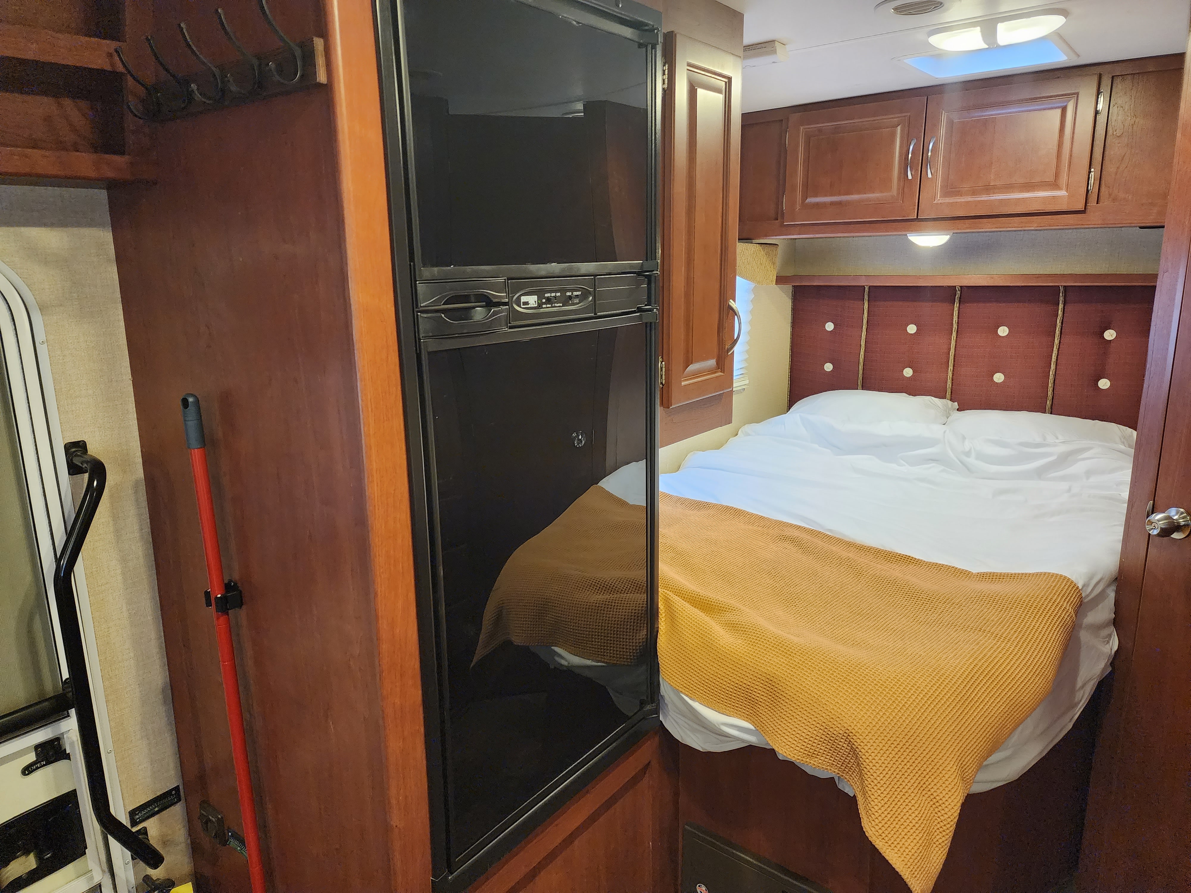 This RV rental offers a compact bedroom with a cozy bed, orange blanket, overhead storage, and a built-in refrigerator.. Winnebago Minnie Winnie 2015
